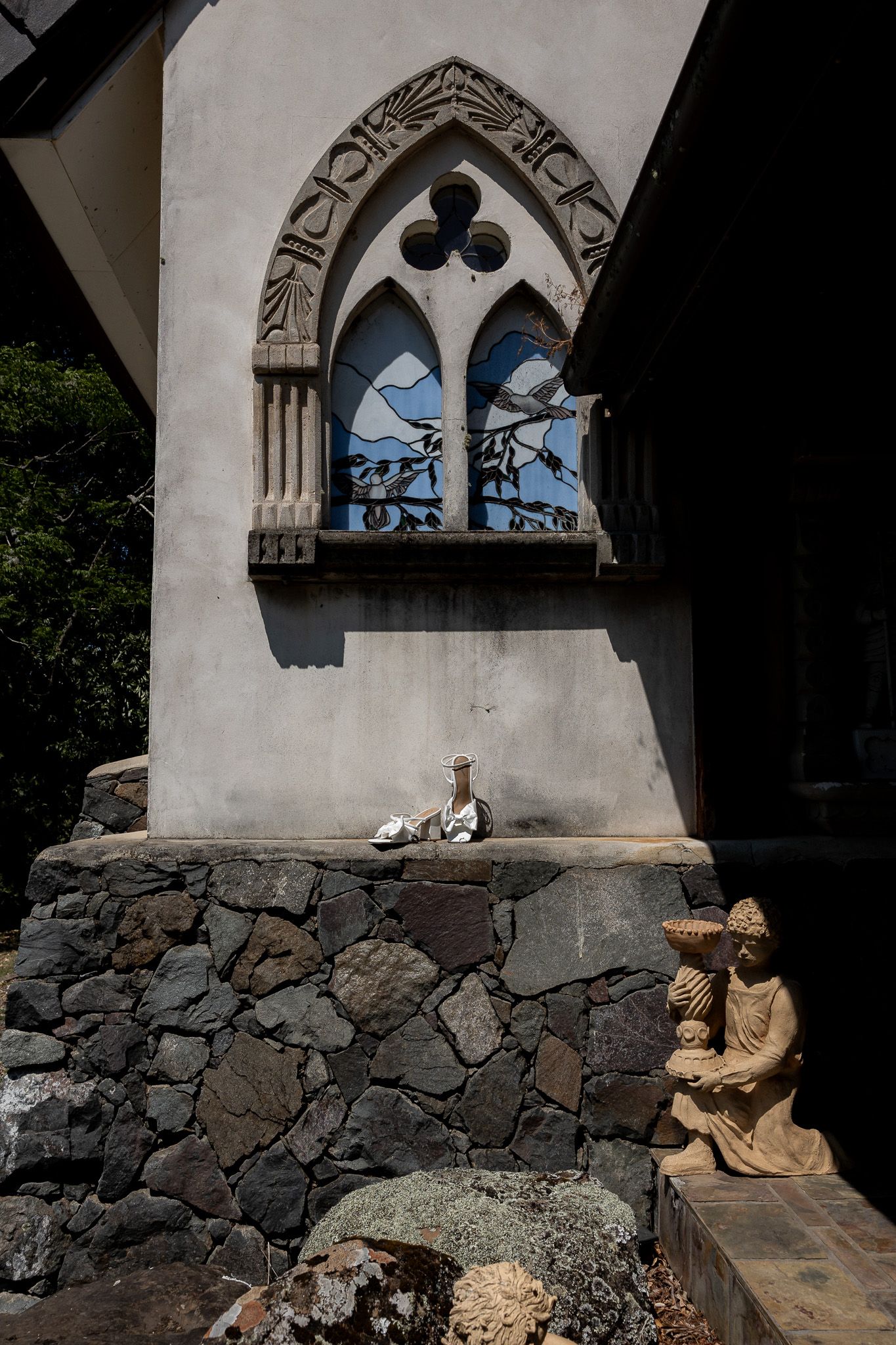 Gothic church window with stone wall and religious statue in sunlight.