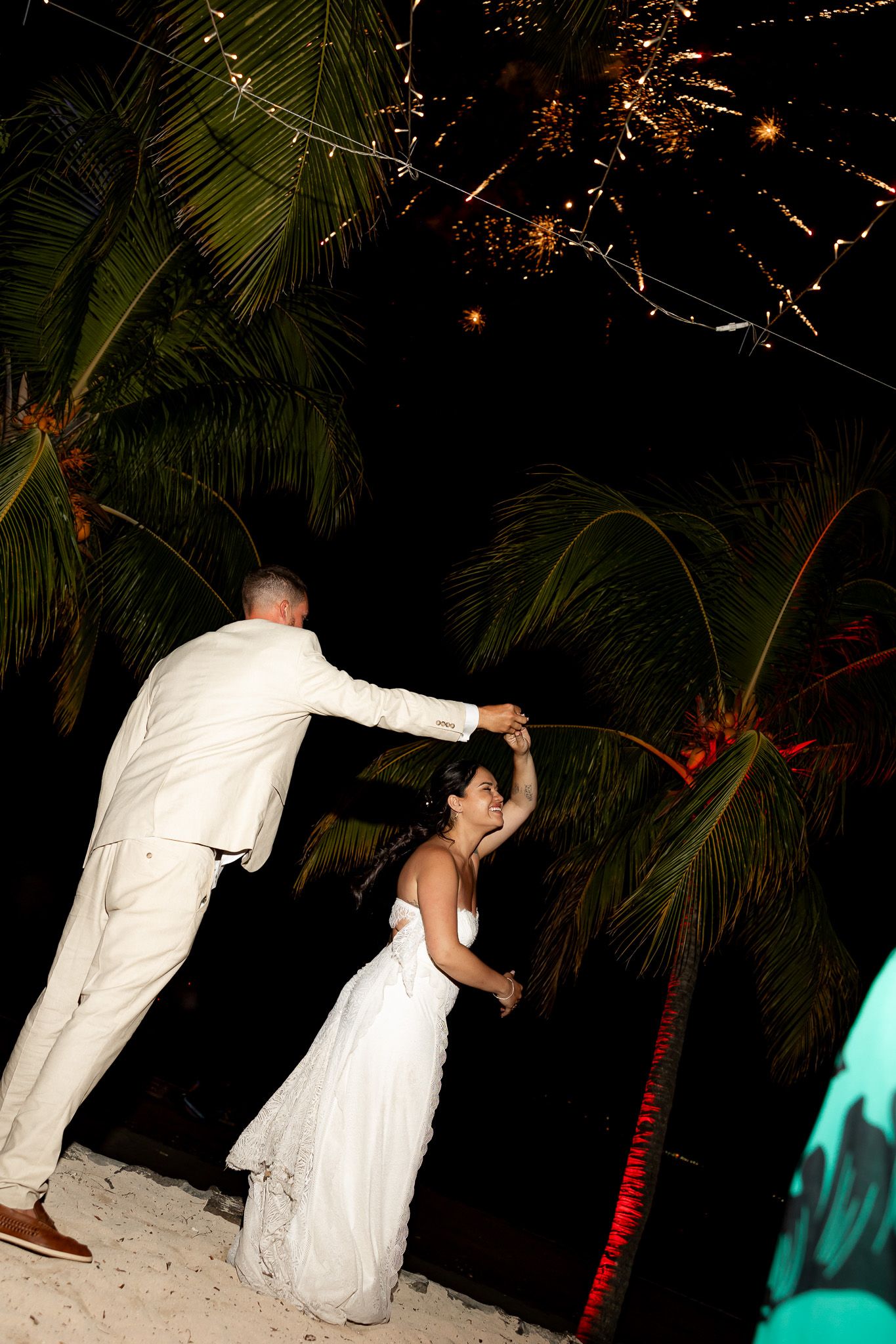 Bride and groom dance under fireworks and palm trees at a romantic tropical beach wedding reception.