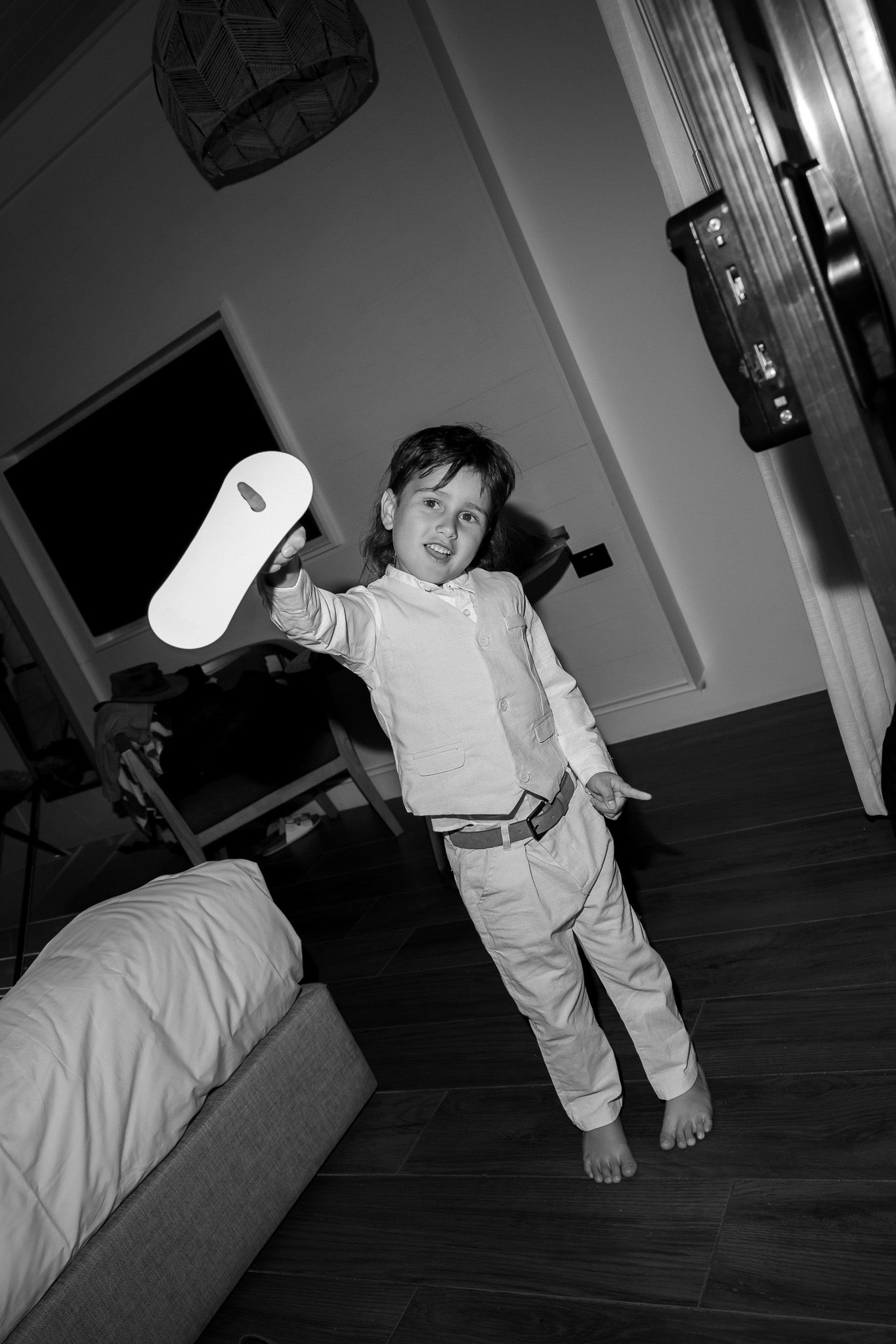 Black and white photo of a young boy holding up a roll of toilet paper indoors.