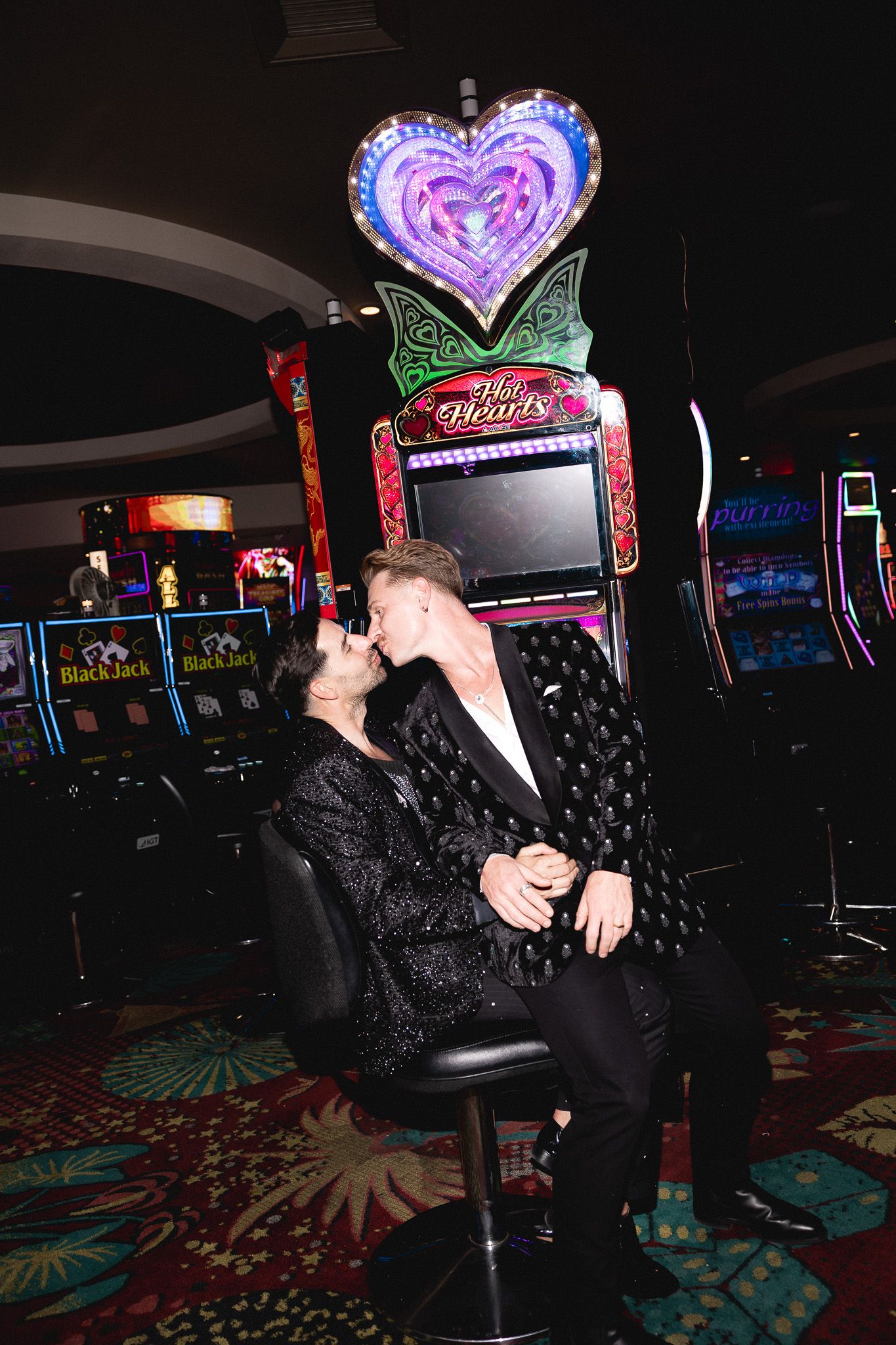 Same-sex couple kisses in front of a Wild Hearts slot machine on a Las Vegas casino floor.