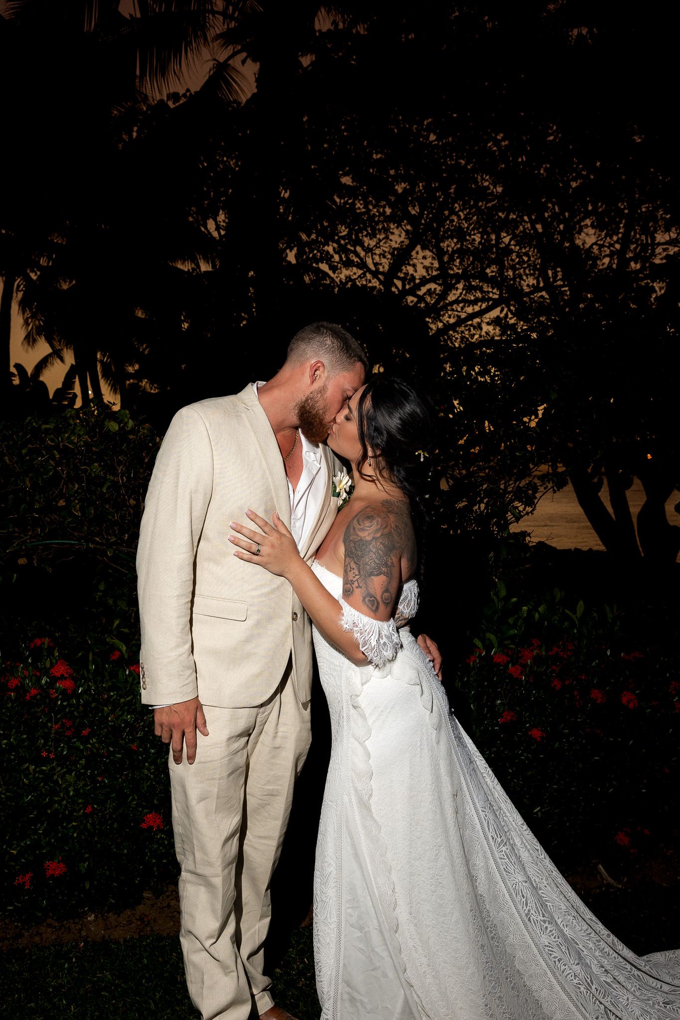Newlyweds share a romantic kiss at sunset surrounded by lush tropical garden greenery.