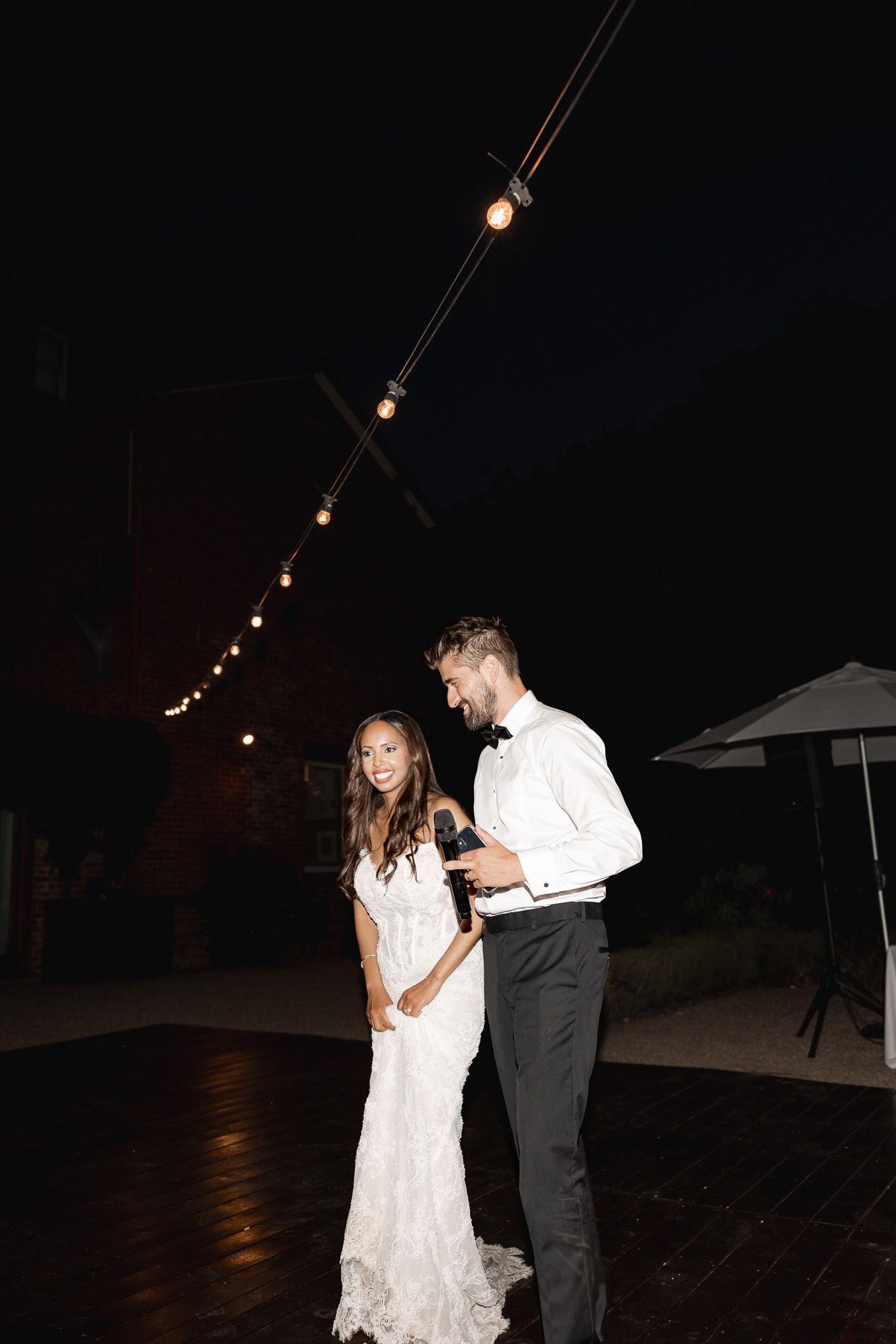 Bride and groom sharing their first dance under string lights at an outdoor evening wedding reception.