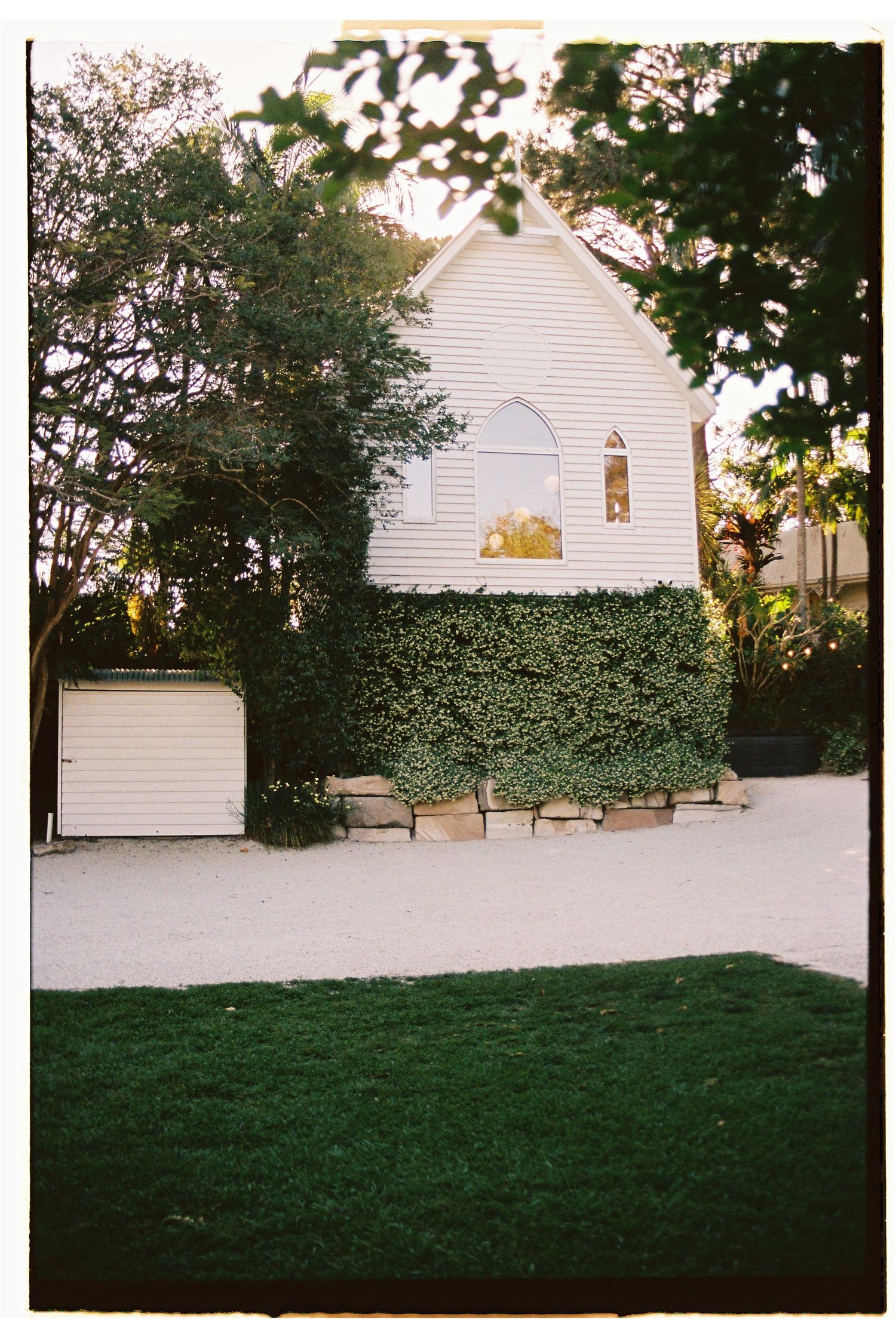 Charming white chapel wedding venue covered in ivy with arched window surrounded by lush green trees.