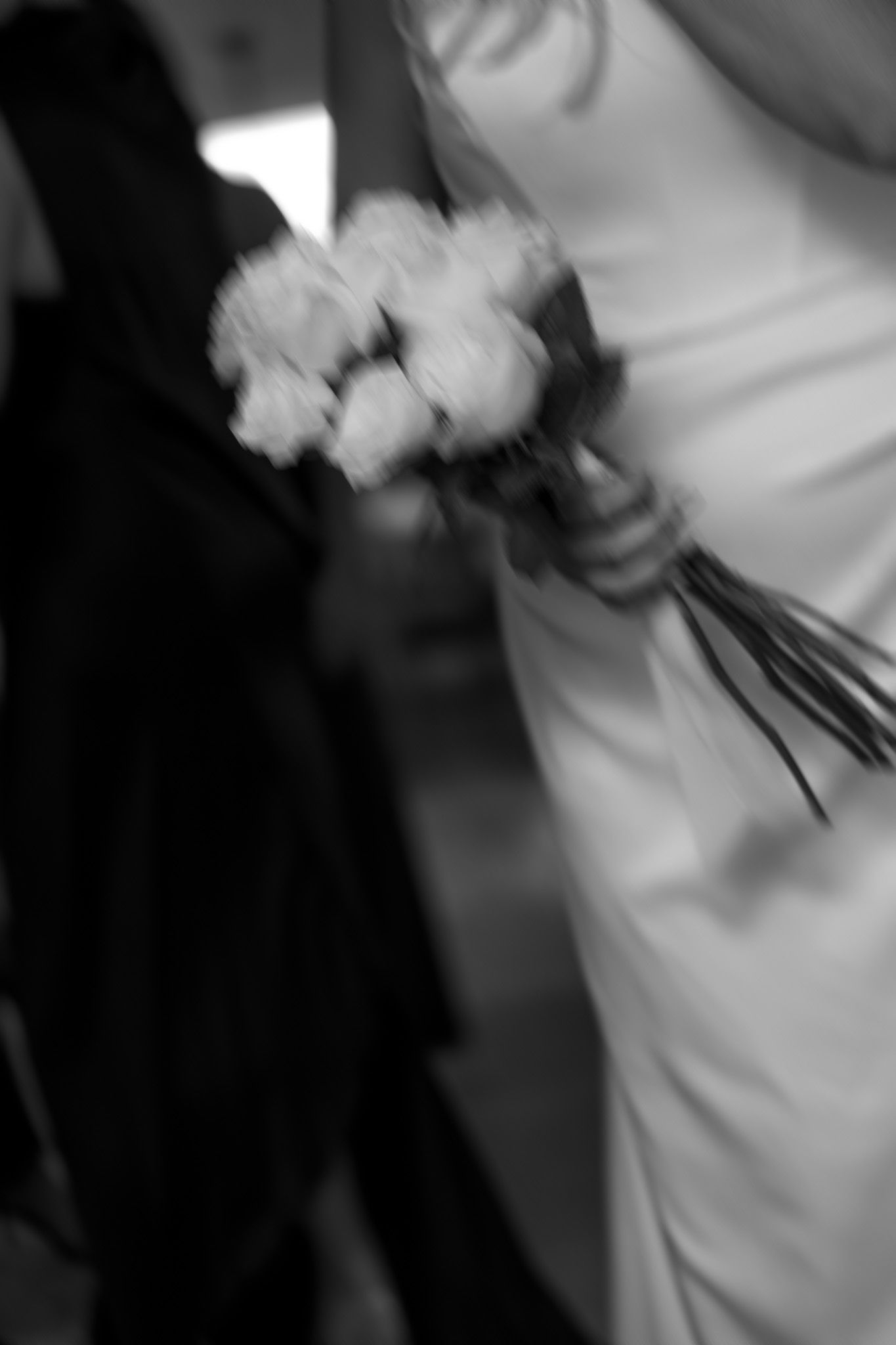 Black and white blurred image of a bride holding a small white rose bouquet in her gown.