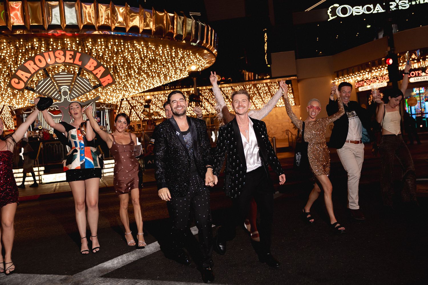 Two grooms in sequin suits dance with guests under bright neon lights on the Las Vegas Strip.