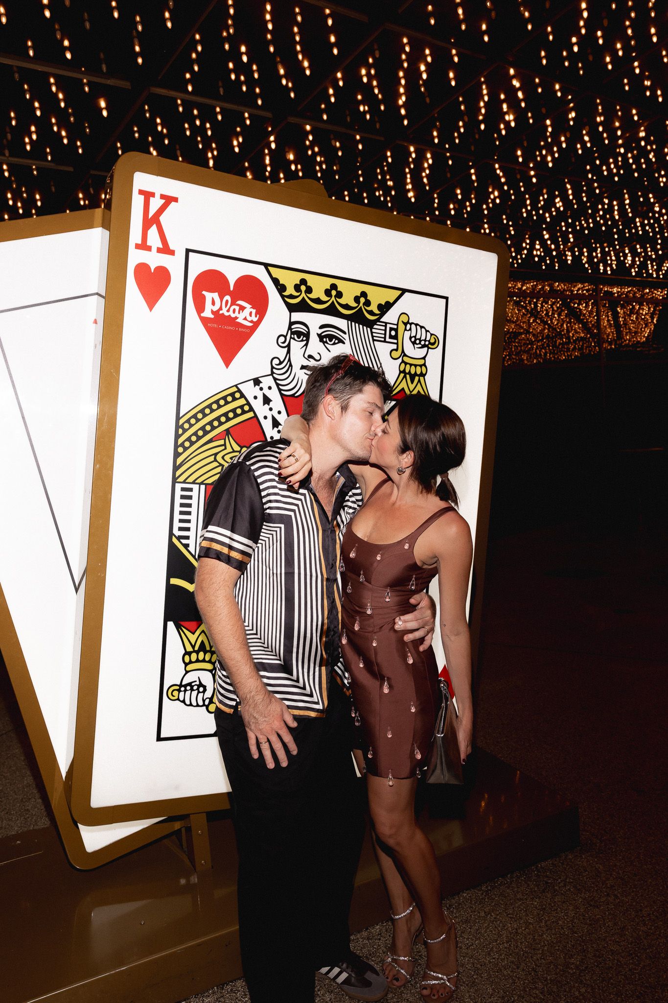 Couple kissing in front of a giant King of Hearts playing card display at a casino-themed event.