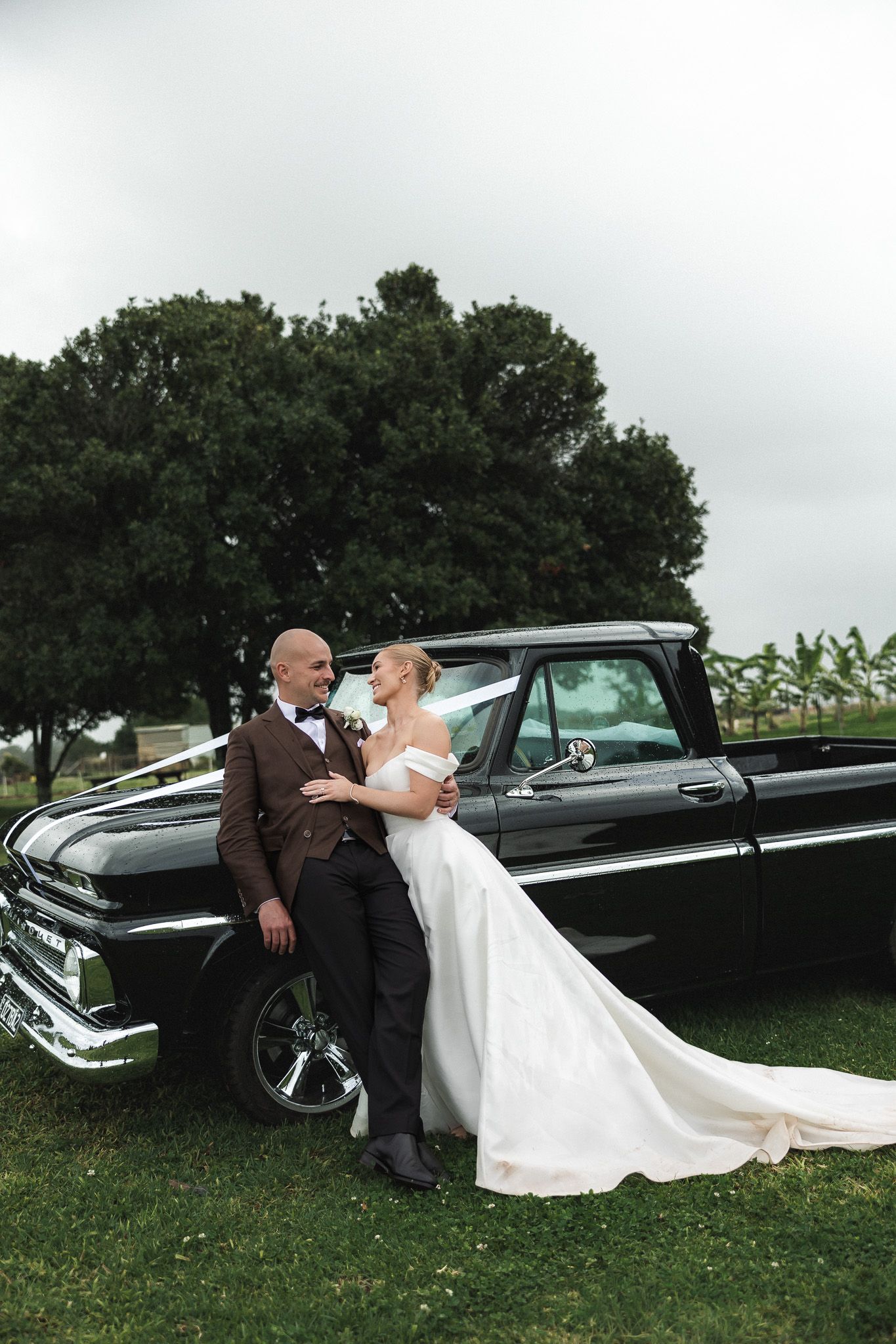 Bride and groom posing romantically against a classic black vintage pickup truck outdoors.