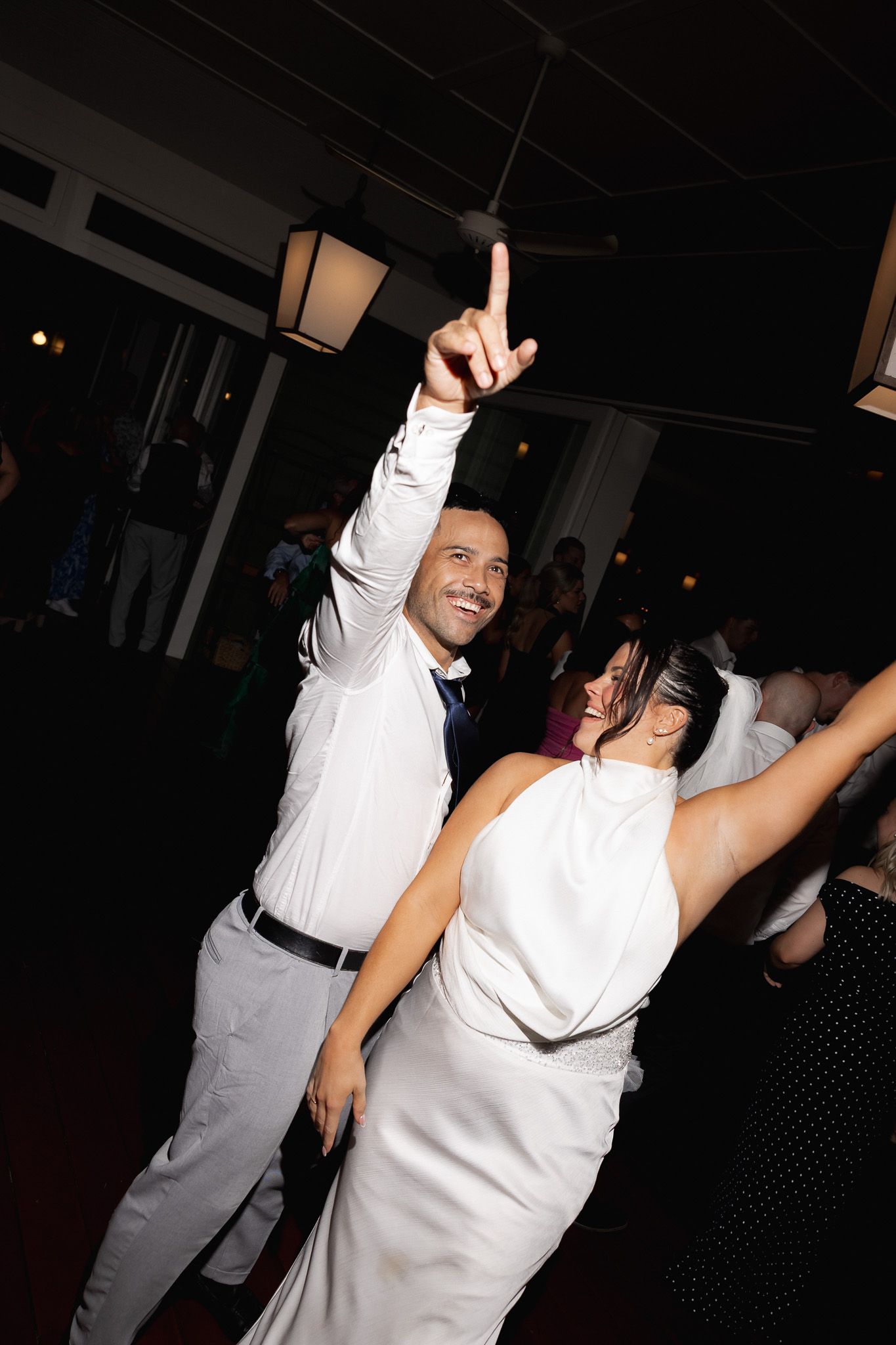 Joyful bride and groom dancing together at their wedding reception with guests celebrating in the background.