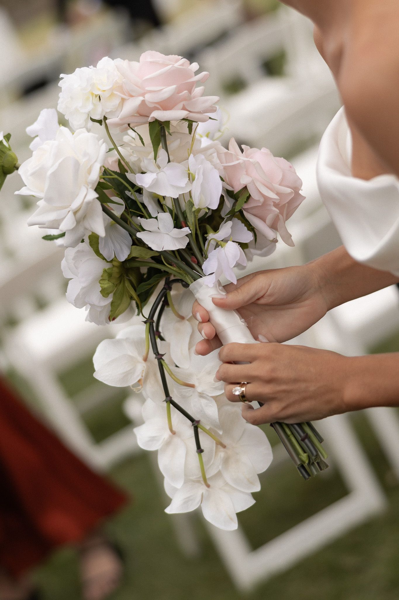 Bride holds cascading bouquet of white and pink roses at wedding ceremony.