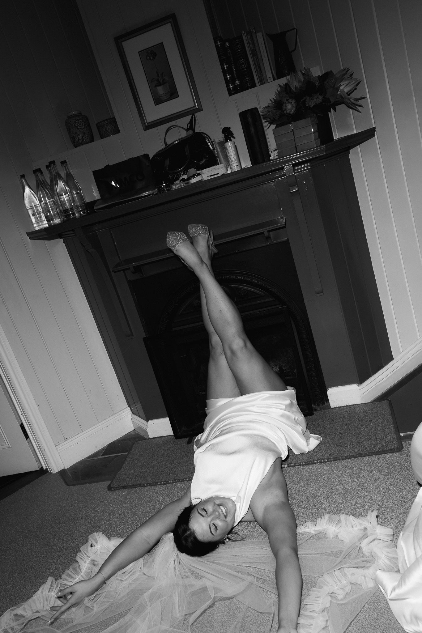 Black and white photo of a bride lying on the floor in her wedding dress with legs raised playfully.