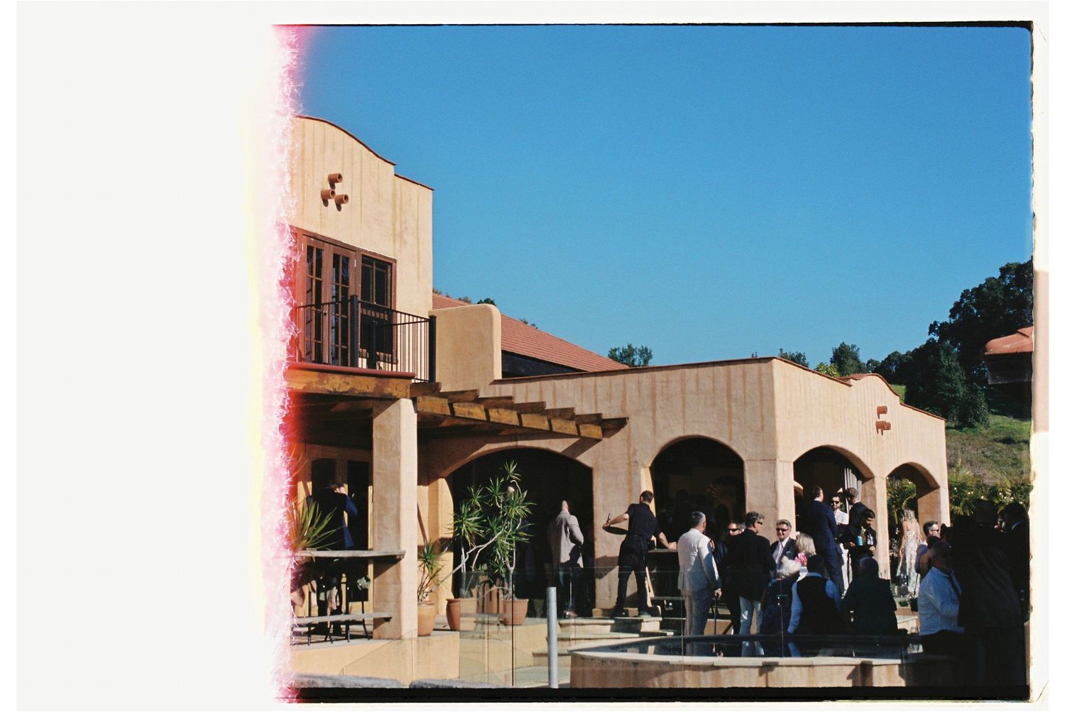 Wedding guests gathering outside a Spanish-style venue with arched doorways on a sunny day.