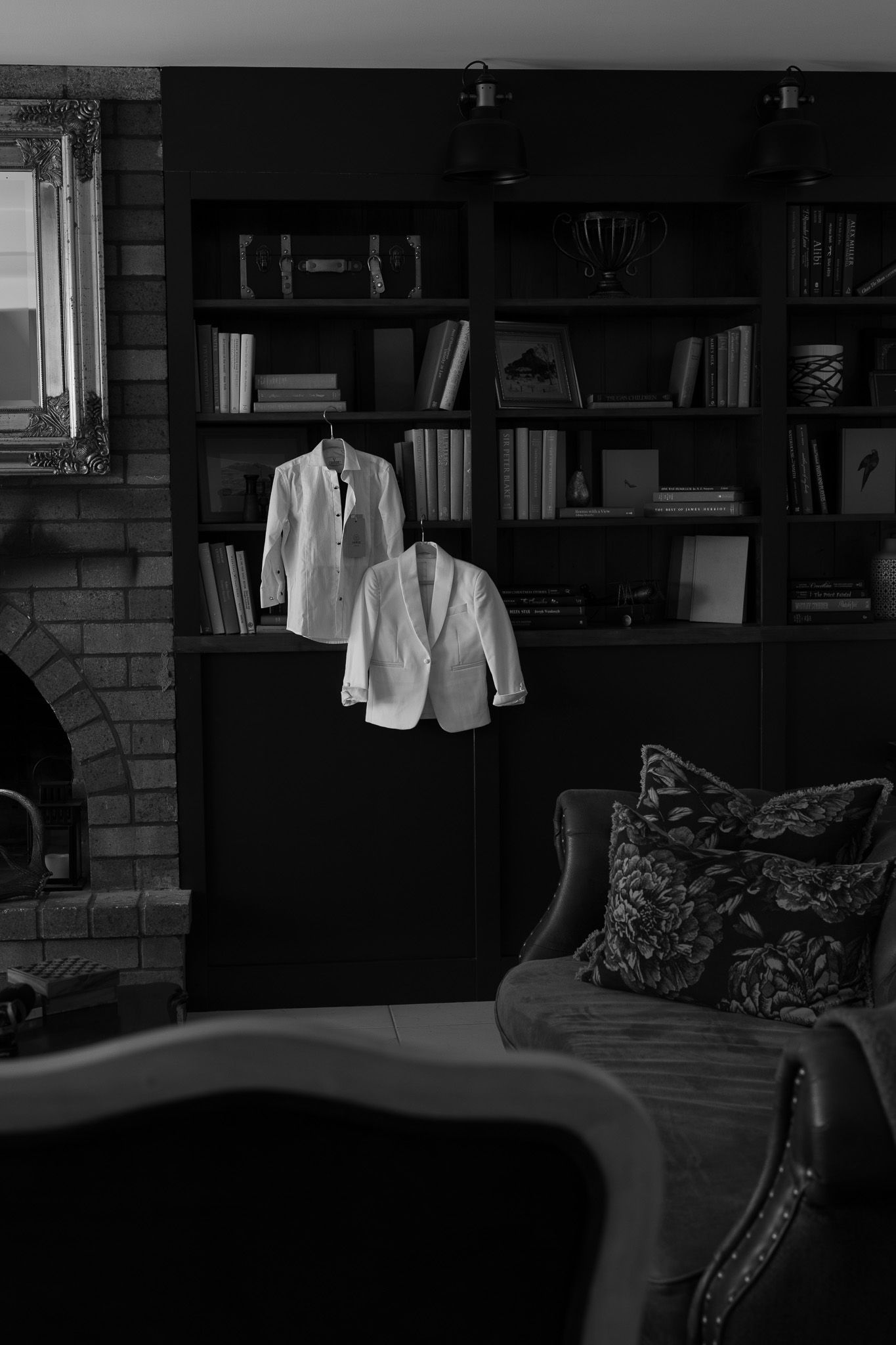 White wedding jackets hanging on bookshelf in dark moody library room in black and white.