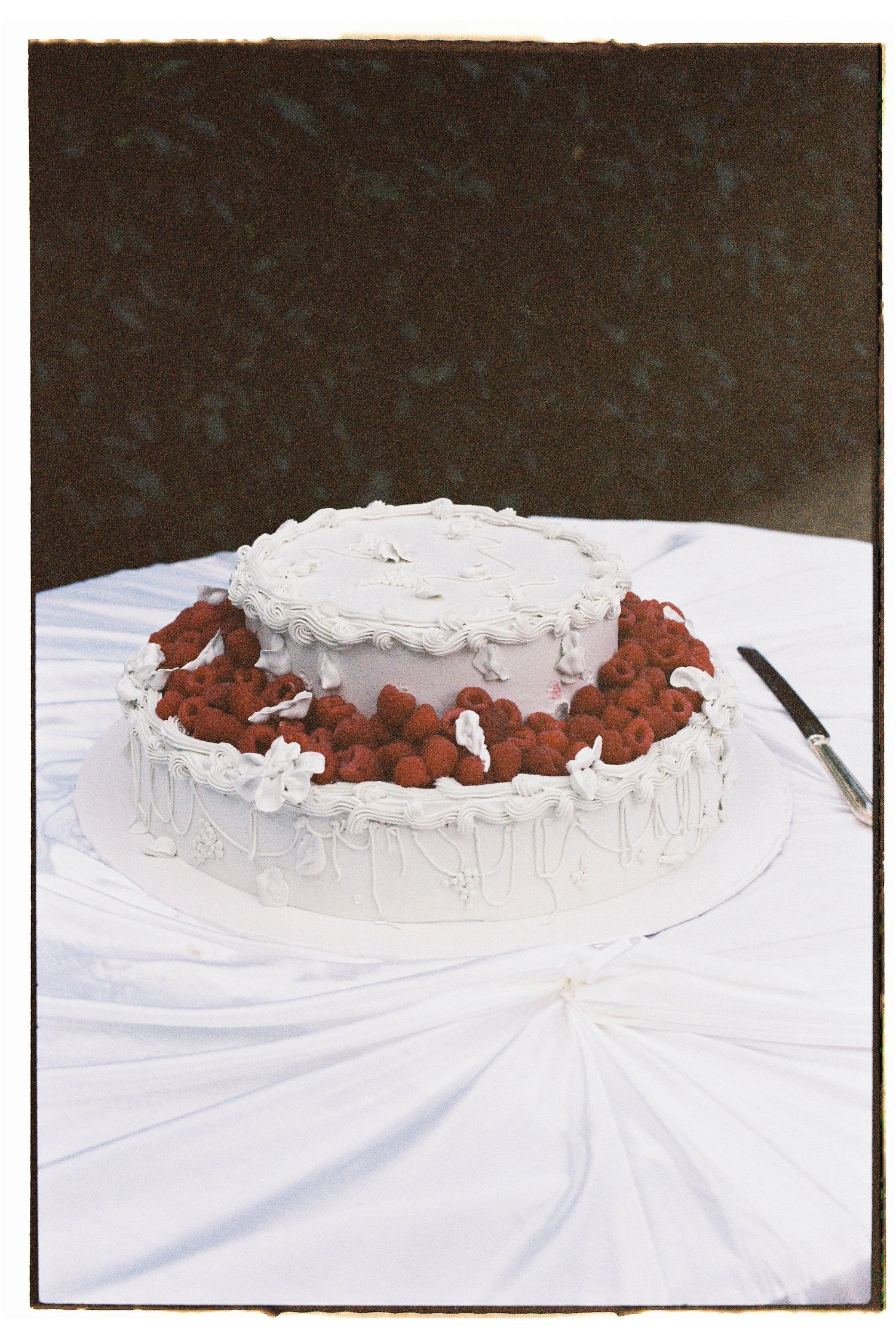 Two-tier white wedding cake decorated with fresh red strawberries on a white draped table.