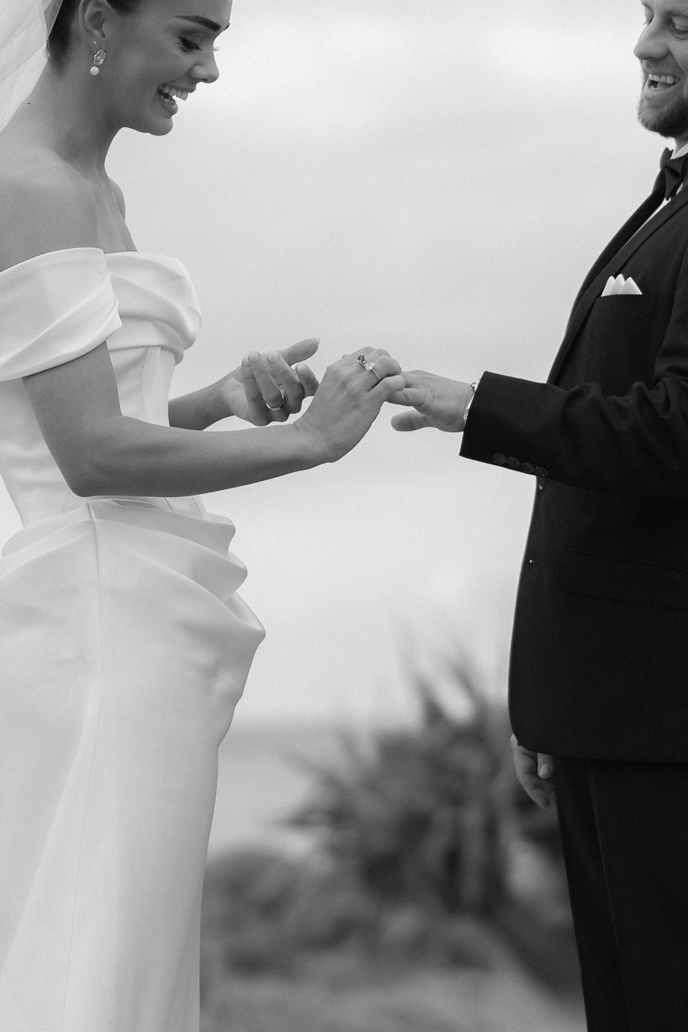 Black and white photo of bride placing wedding ring on grooms finger during ceremony.
