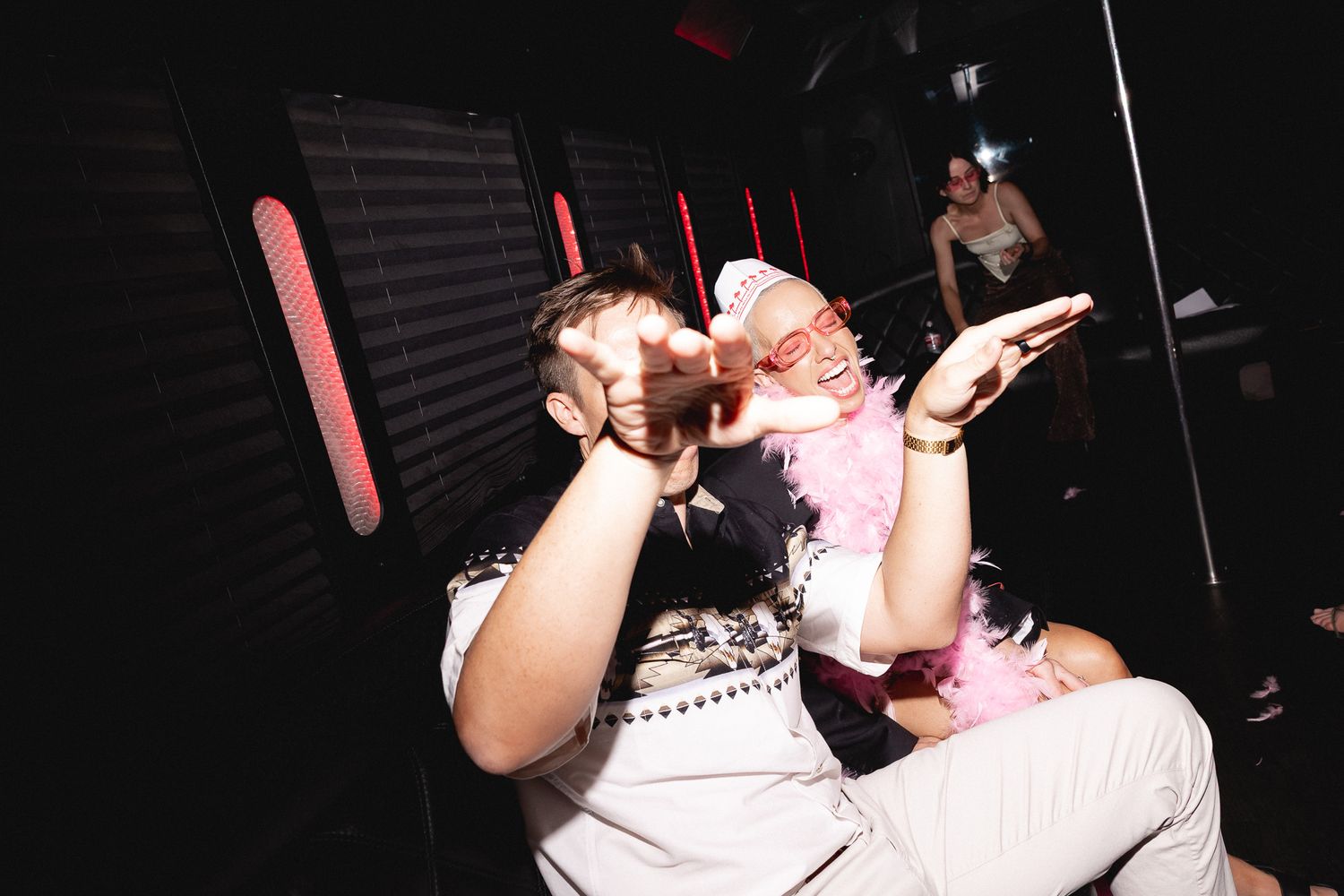 Two people celebrate at a dark nightclub, one drinking from a bottle while wearing festive accessories.