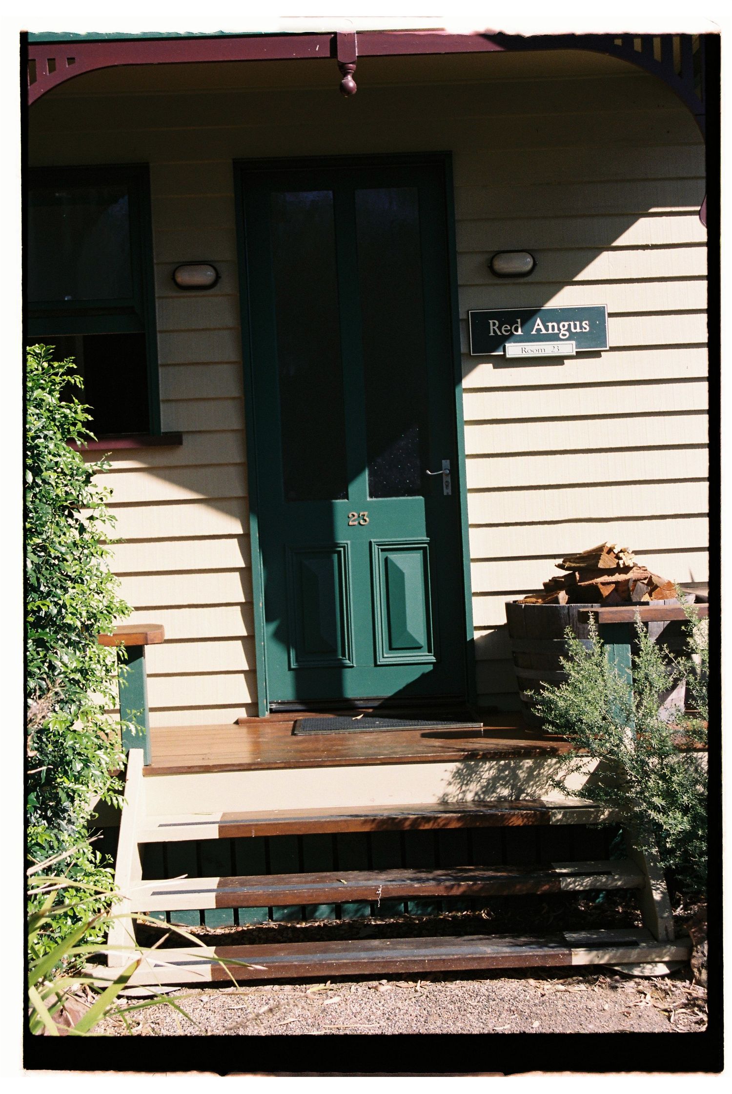 Green door entrance to Red Angus cottage number 23 with wooden steps and lush garden surrounds.