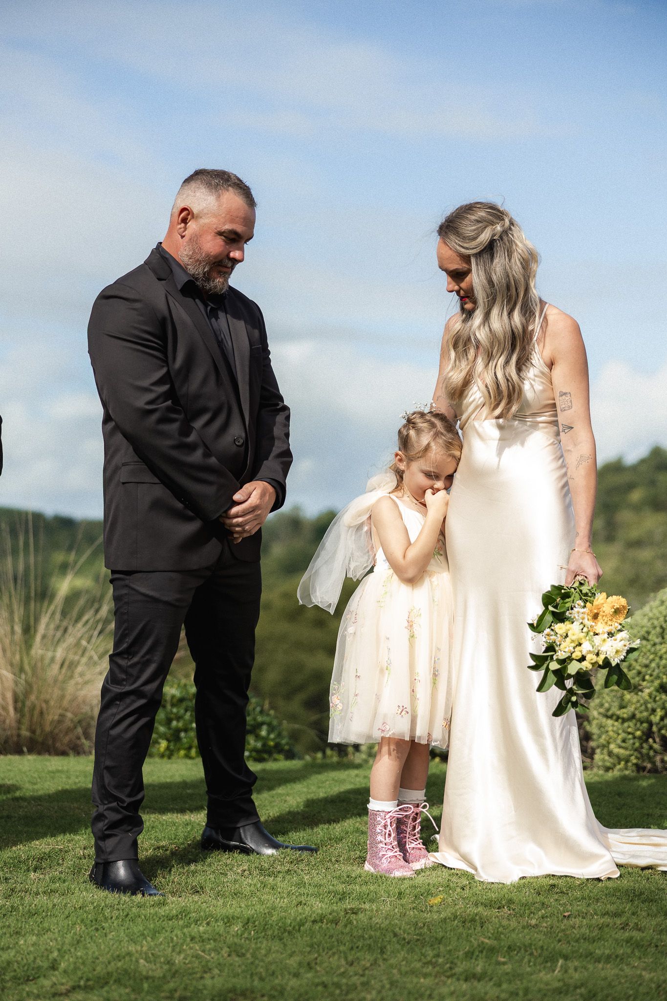 Groom in black suit and bride in ivory gown with flower girl at ceremony.