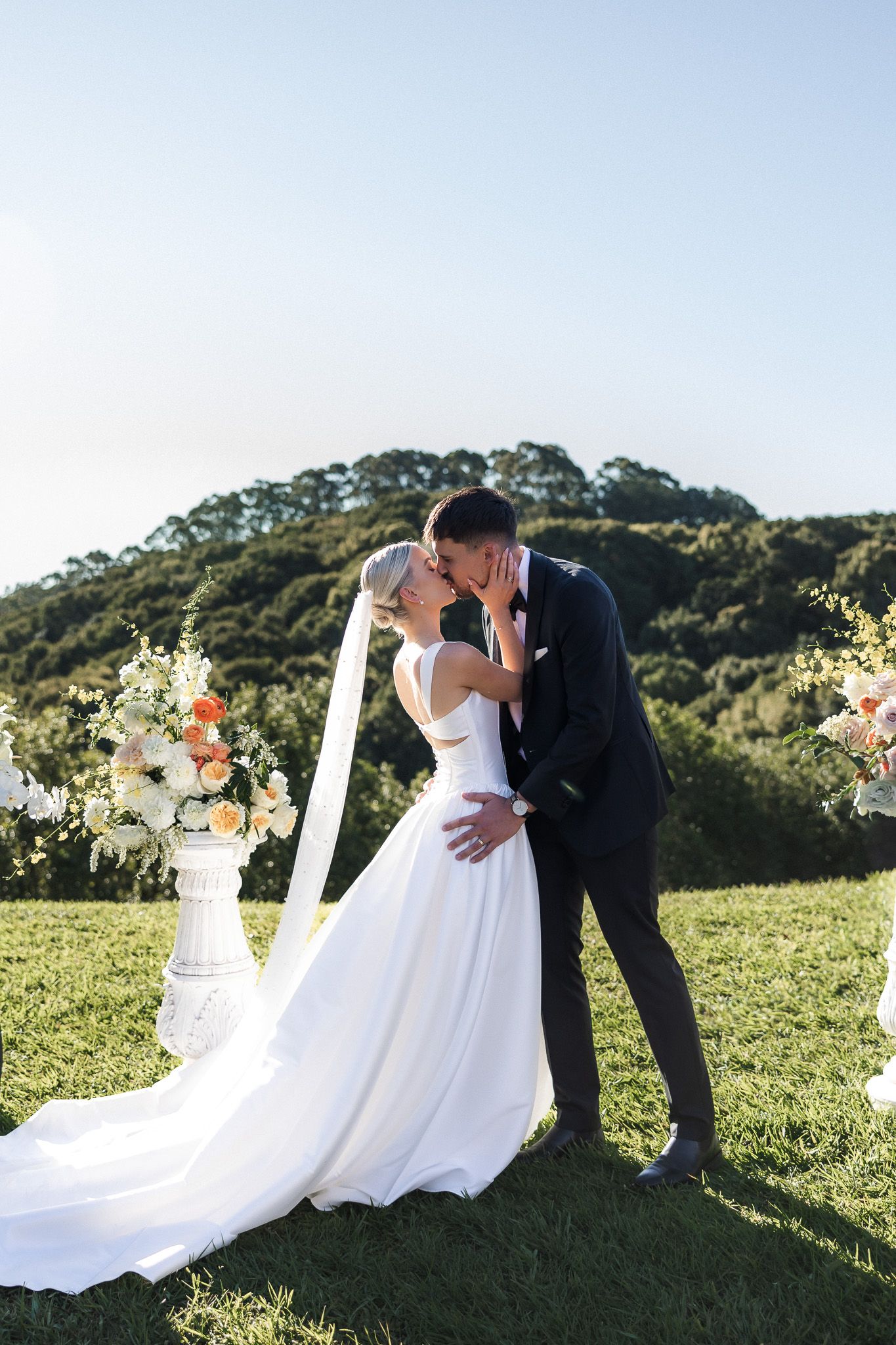 Bride and groom share their first kiss at an outdoor wedding ceremony with rolling hills backdrop.