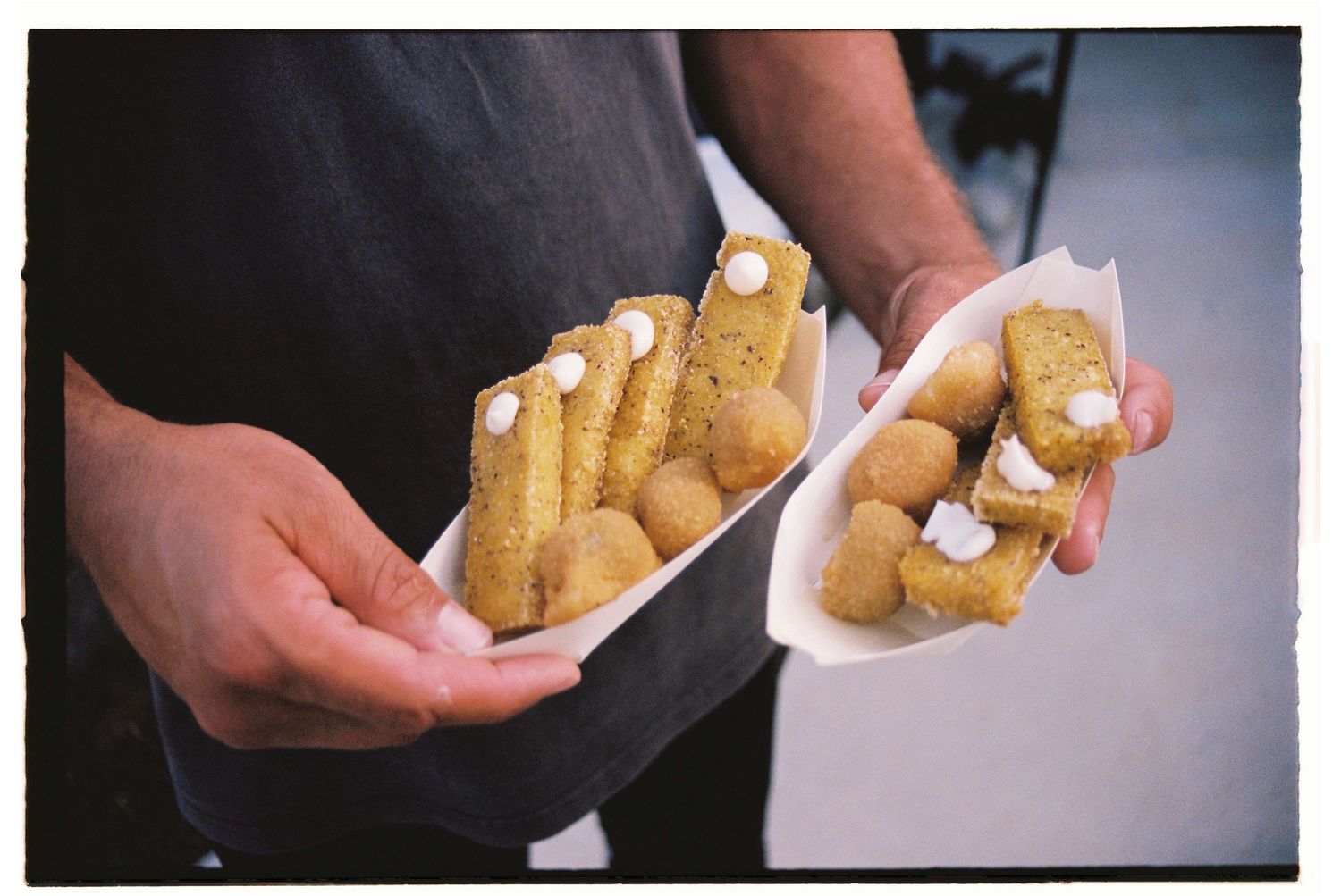 Server holding two paper boats filled with golden fried snacks and cream at catering event.