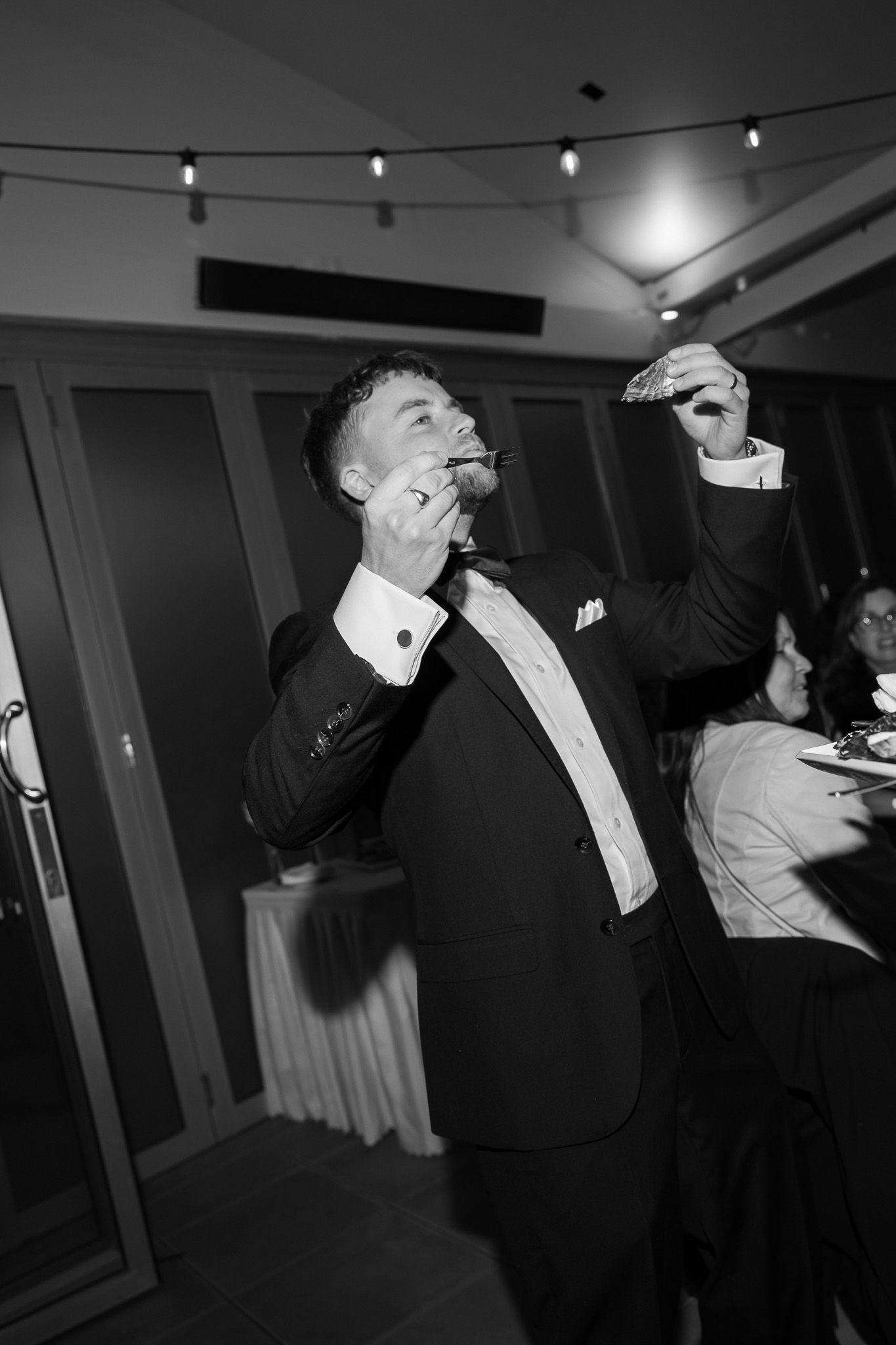 Groom celebrating at wedding reception in black and white photo, raising glass and laughing.