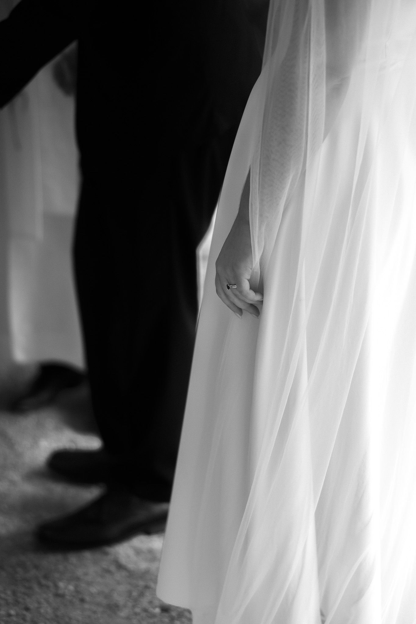 Black and white photo of bride and groom holding hands, wedding dress veil flowing, formal shoes visible.