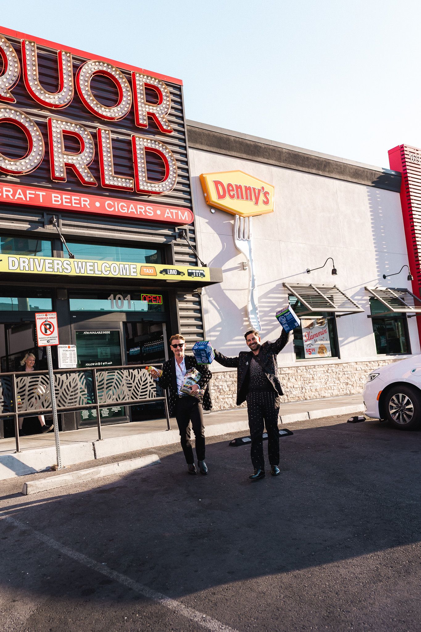 Two men pose outside Denny's restaurant and Liquor World store in Las Vegas, holding items aloft.