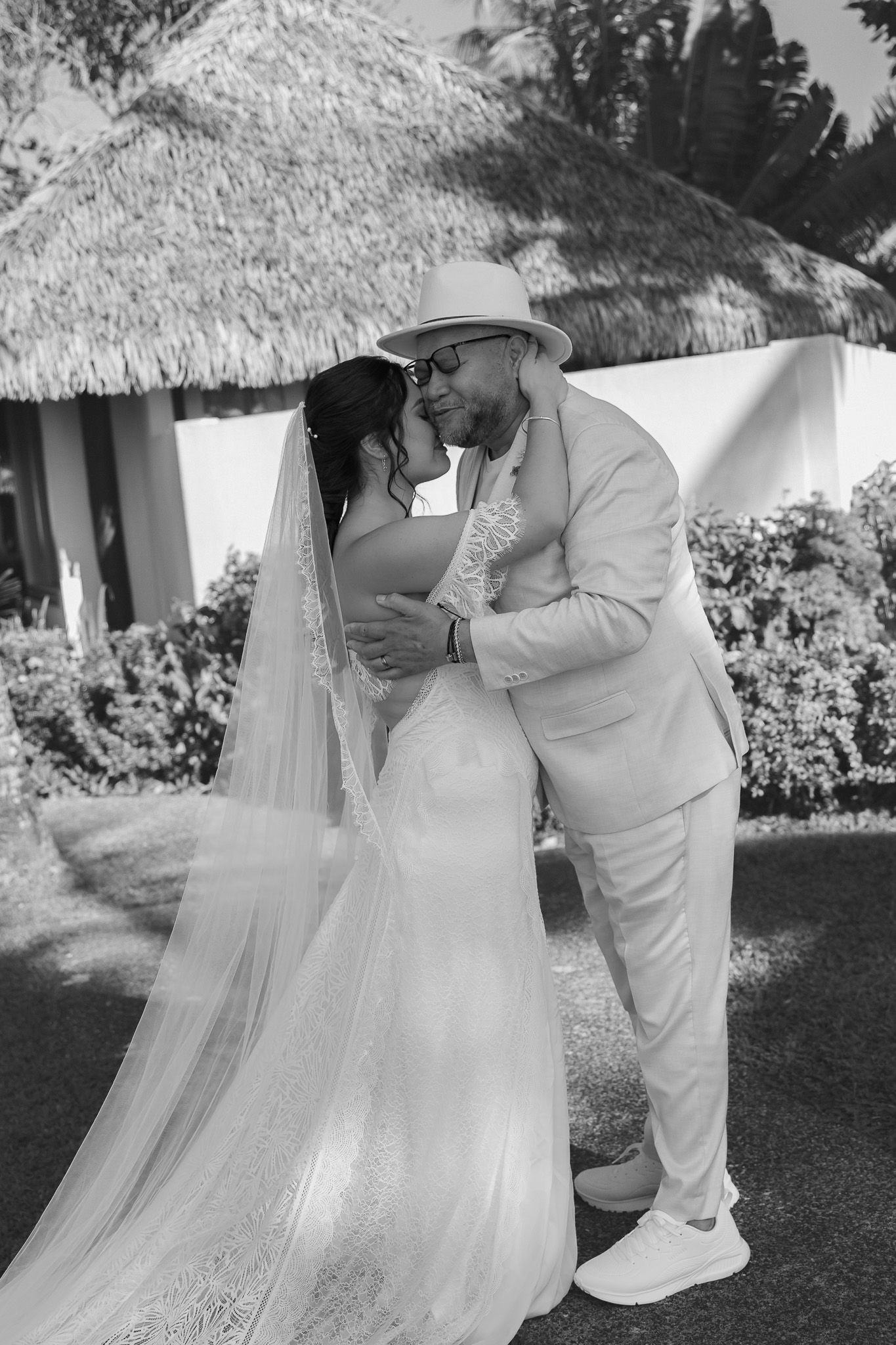 Black and white photo of bride and groom sharing romantic embrace at tropical outdoor wedding venue.