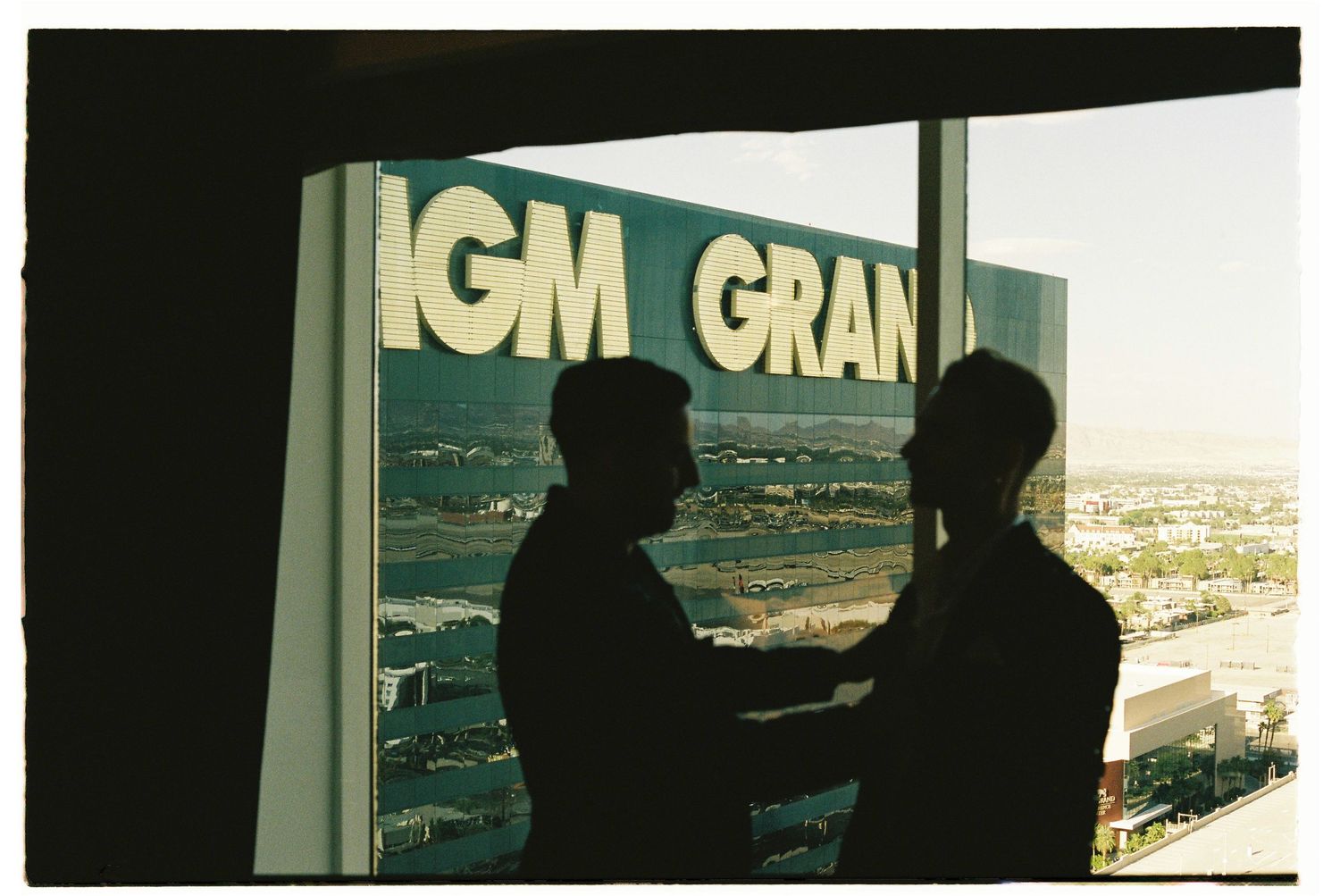 Two silhouetted figures shaking hands in front of the MGM Grand sign with Las Vegas cityscape backdrop.
