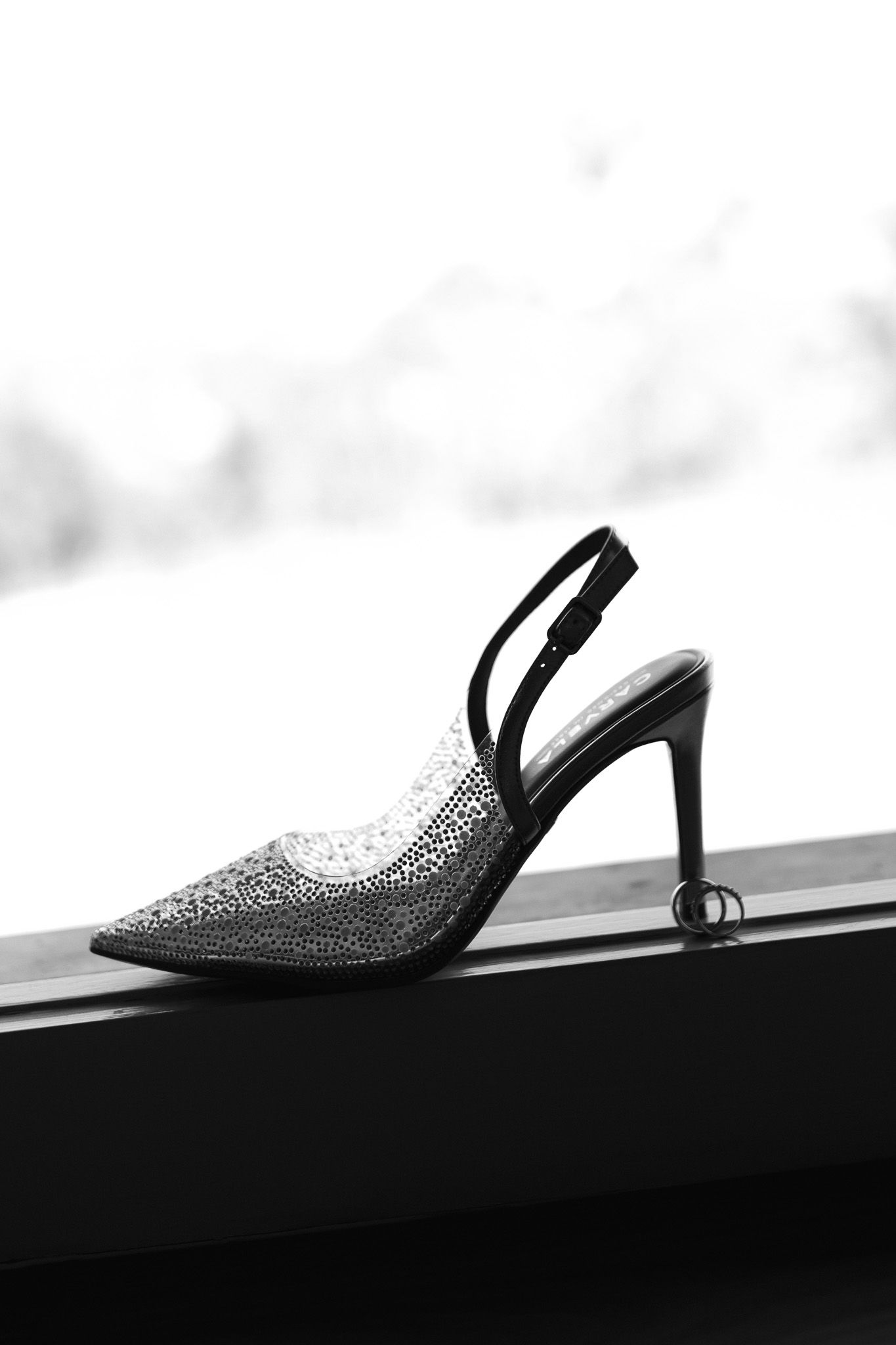 Elegant black slingback stiletto heel with crystal embellishments displayed on a windowsill in black and white.