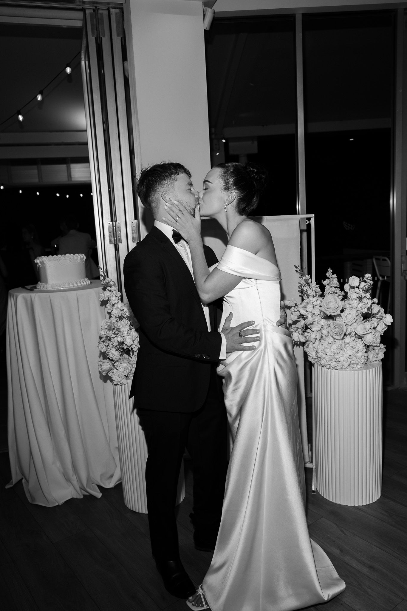 Black and white photo of bride and groom sharing first kiss at reception.