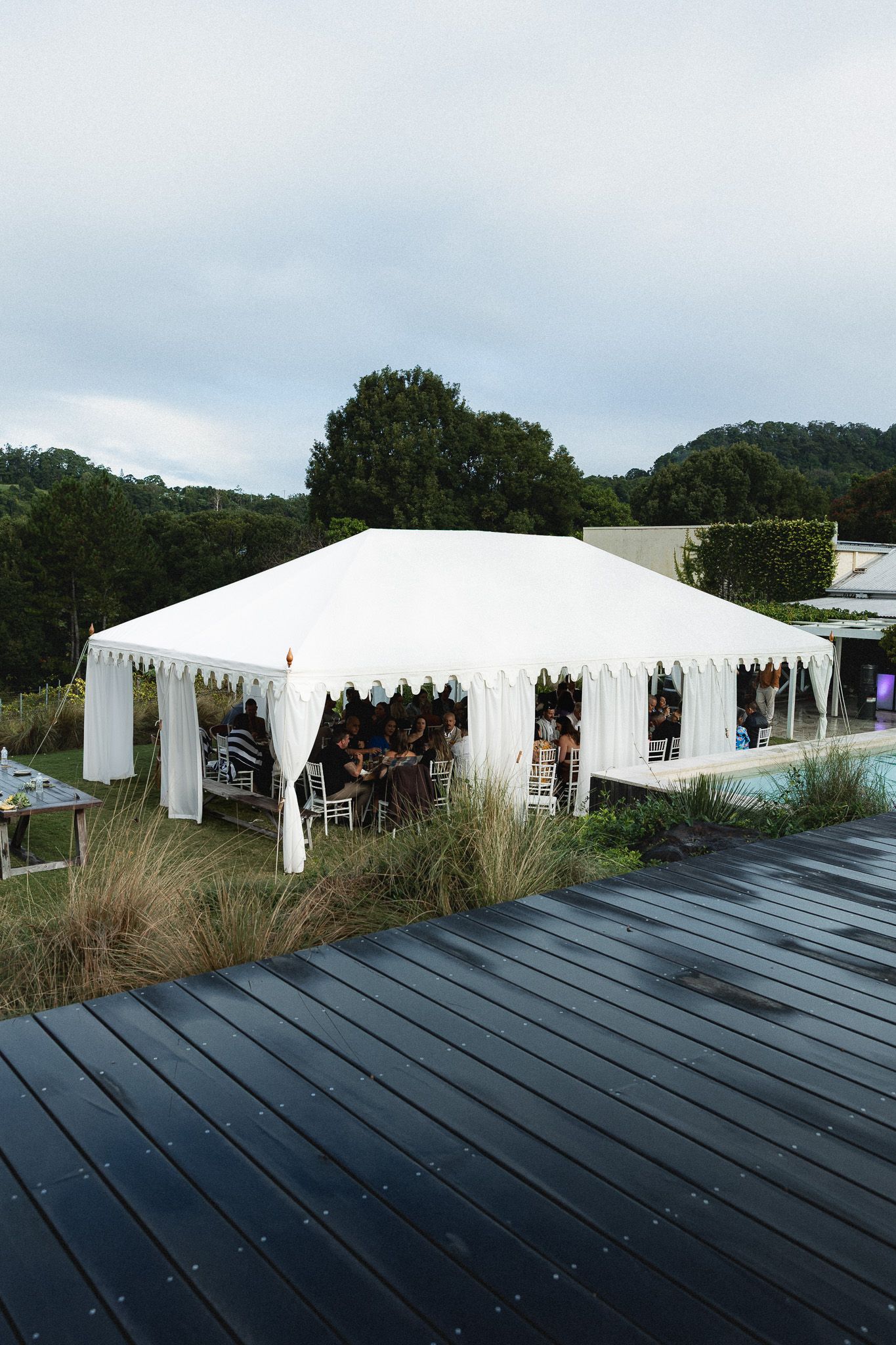 A white wedding marquee tent set up outdoors with guests dining inside at a reception.
