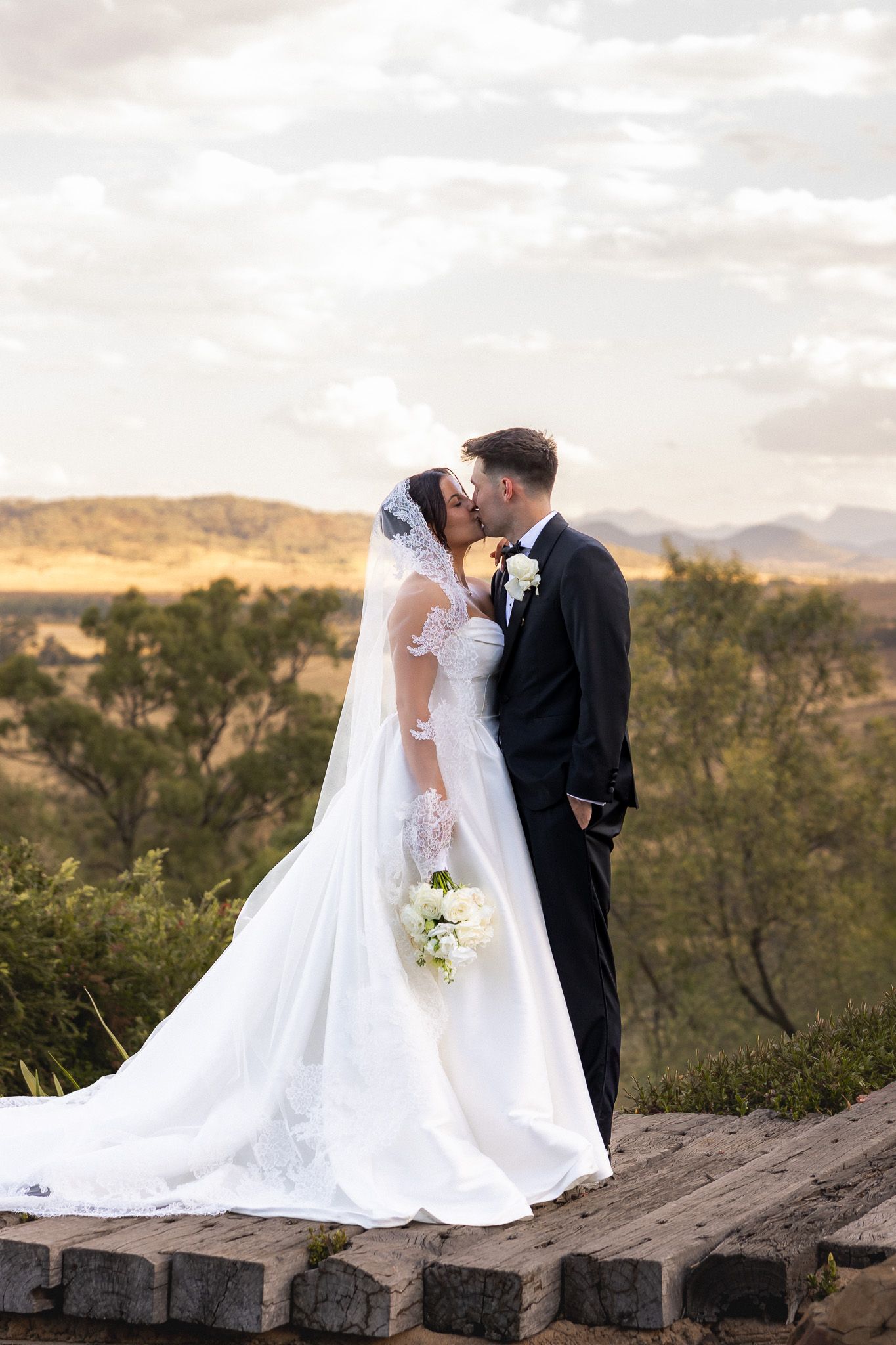 Bride and groom kissing with a scenic landscape backdrop at their outdoor wedding.