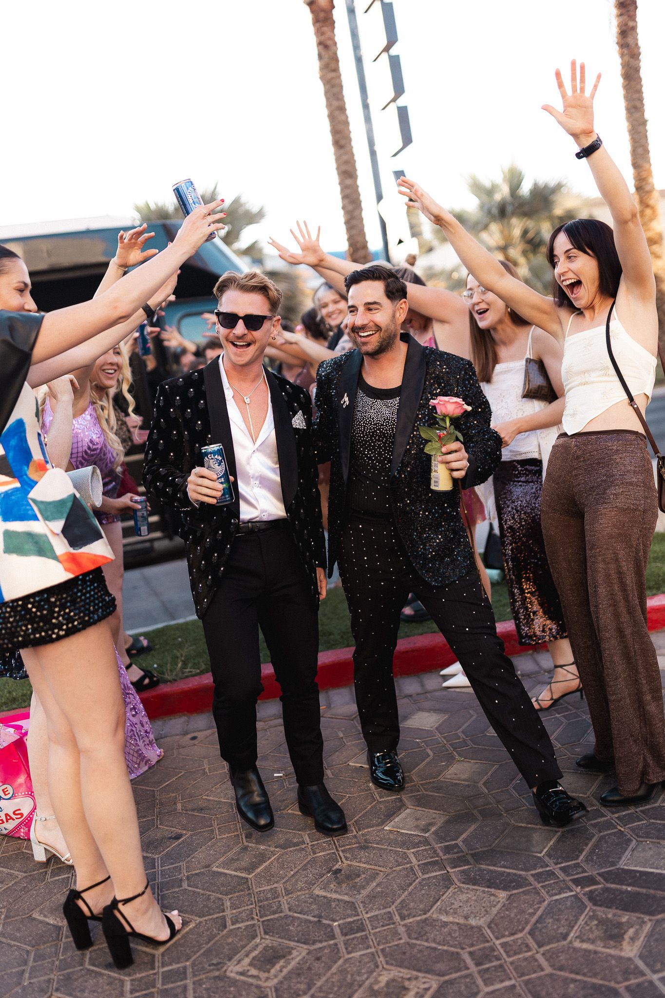 Two grooms in sparkly black suits celebrate with cheering guests at a Las Vegas wedding.