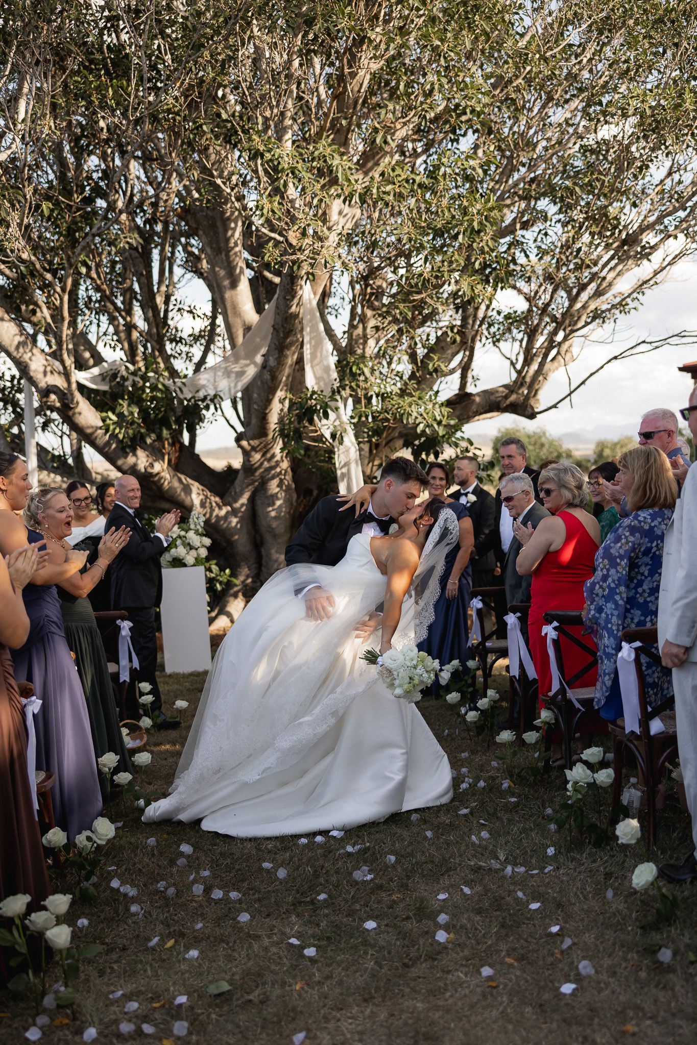 Bride and groom sharing a romantic dip kiss at their outdoor wedding ceremony.