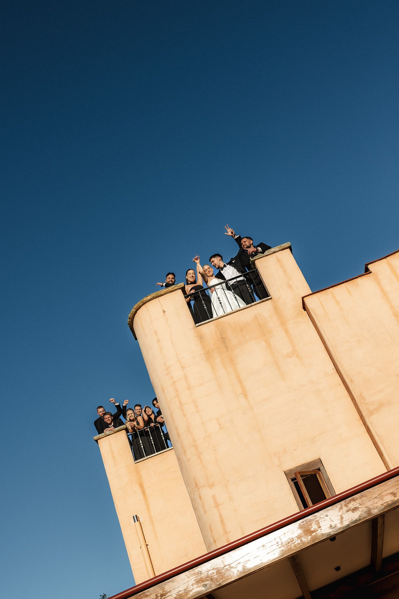 Wedding party celebrates on a rooftop terrace against a vivid blue sky at golden hour.
