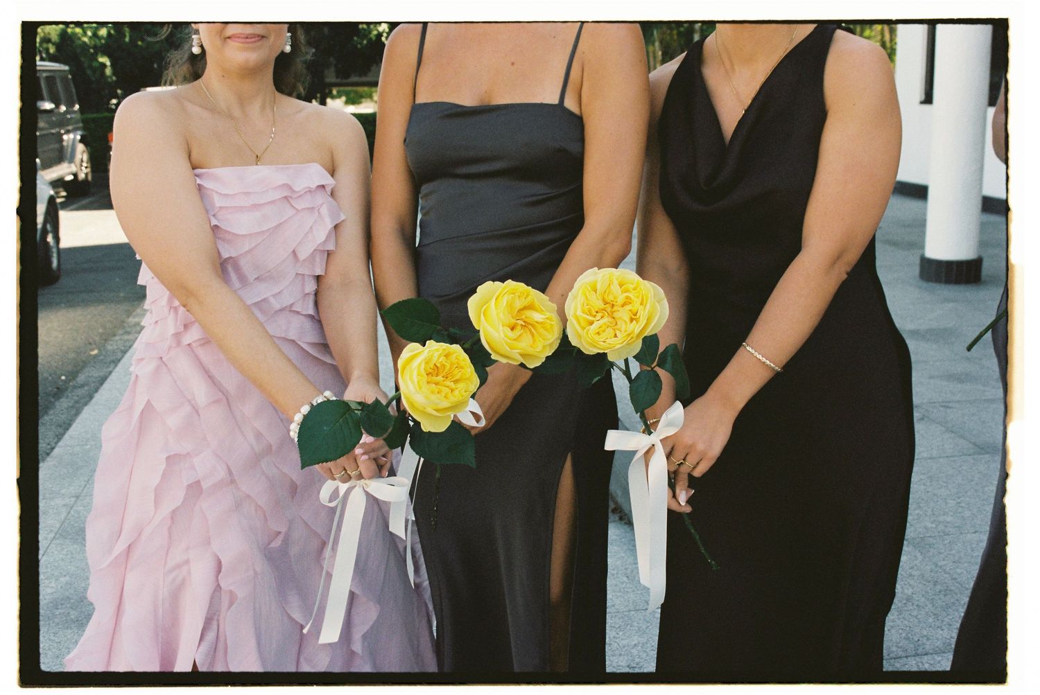 Three bridesmaids in pink and black dresses holding yellow rose bouquets.