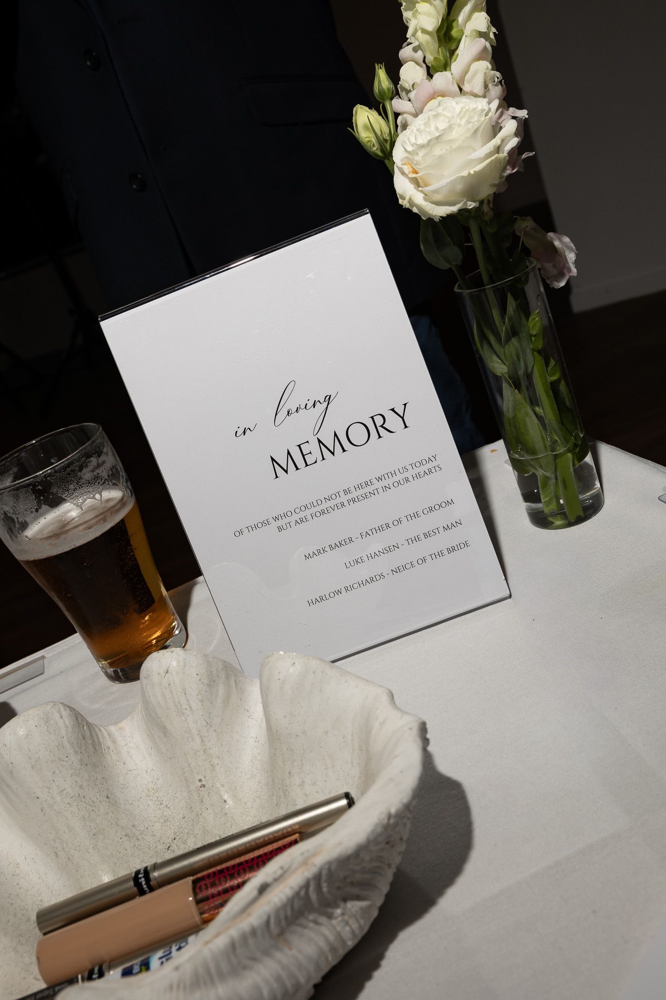 Elegant wedding memory table with white roses, a beer glass, and an in loving memory sign honoring deceased loved ones.