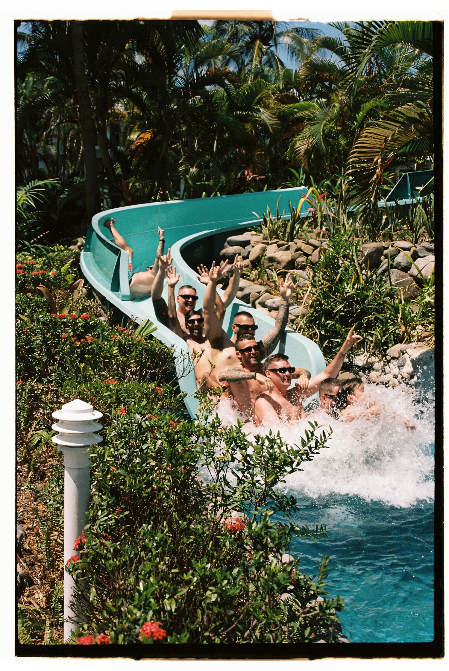 Excited group of people riding a water slide attraction surrounded by tropical palm trees at a sunny water park.