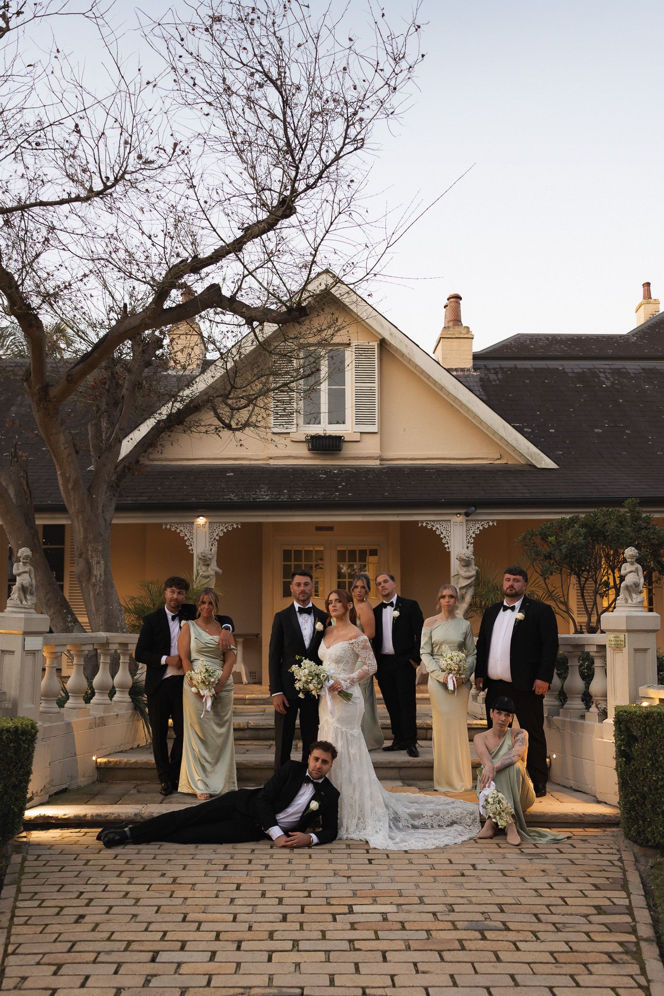 Wedding party posing in front of a classic yellow house at dusk.