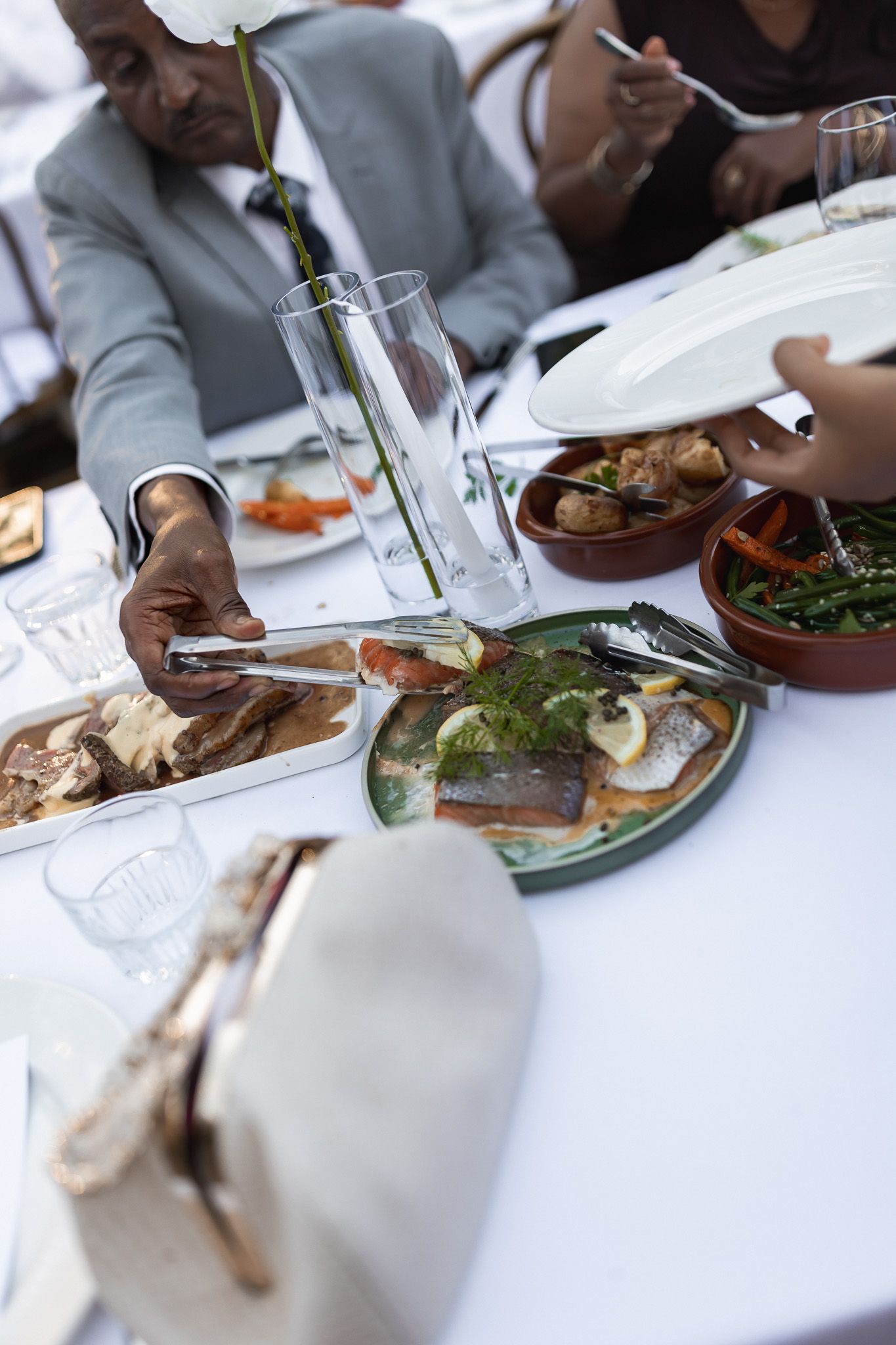 Wedding guests sharing platters of salmon and bread at an elegant outdoor reception dinner table.