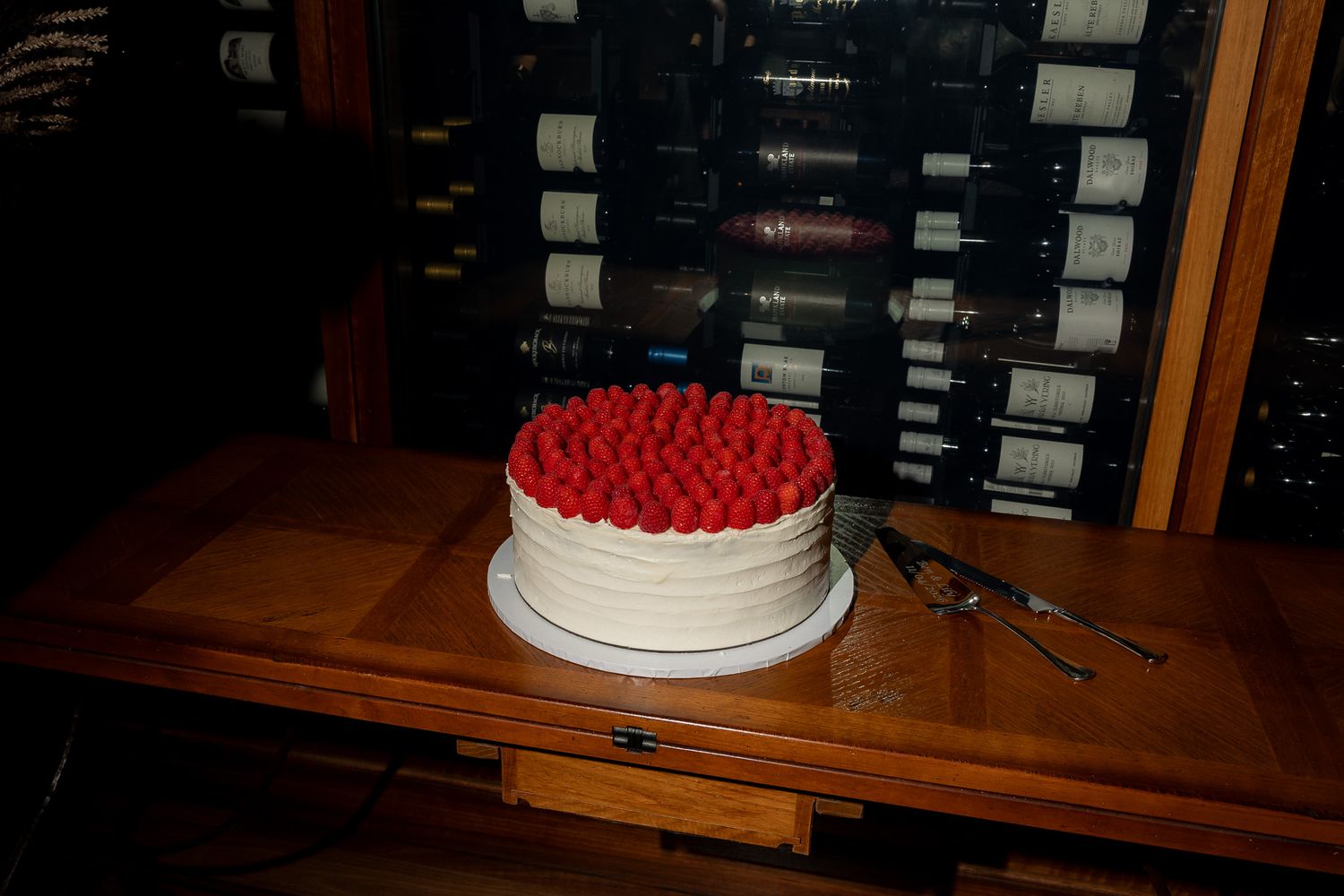 White wedding cake topped with fresh red raspberries displayed on a wooden table.