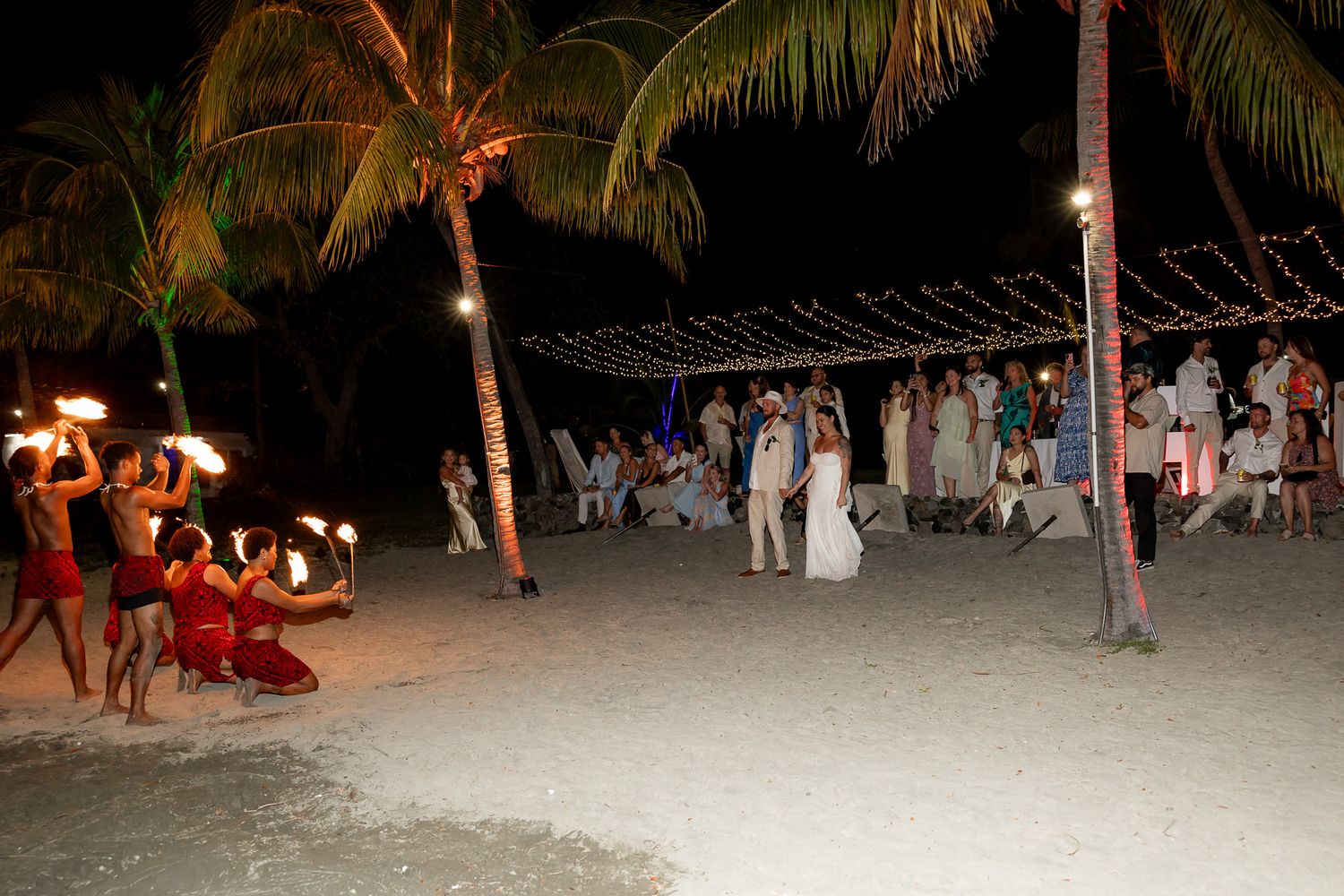 Fire dancers performing on beach during tropical outdoor wedding reception at night.