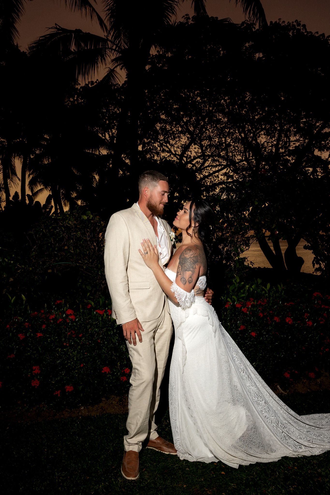 Bride and groom sharing romantic moment at night surrounded by tropical garden and palm trees.