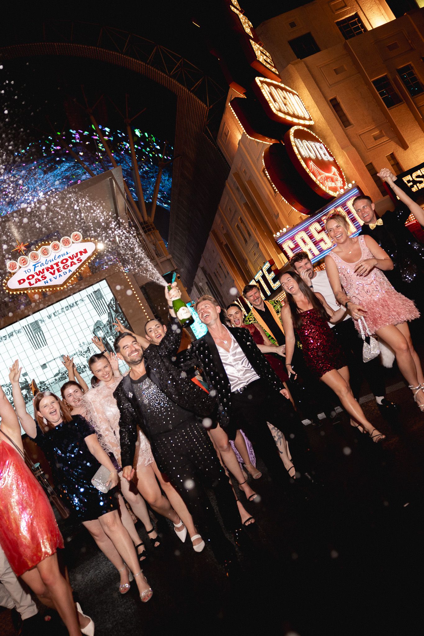 Wedding party celebrates under neon lights at the Welcome to Las Vegas sign at night.