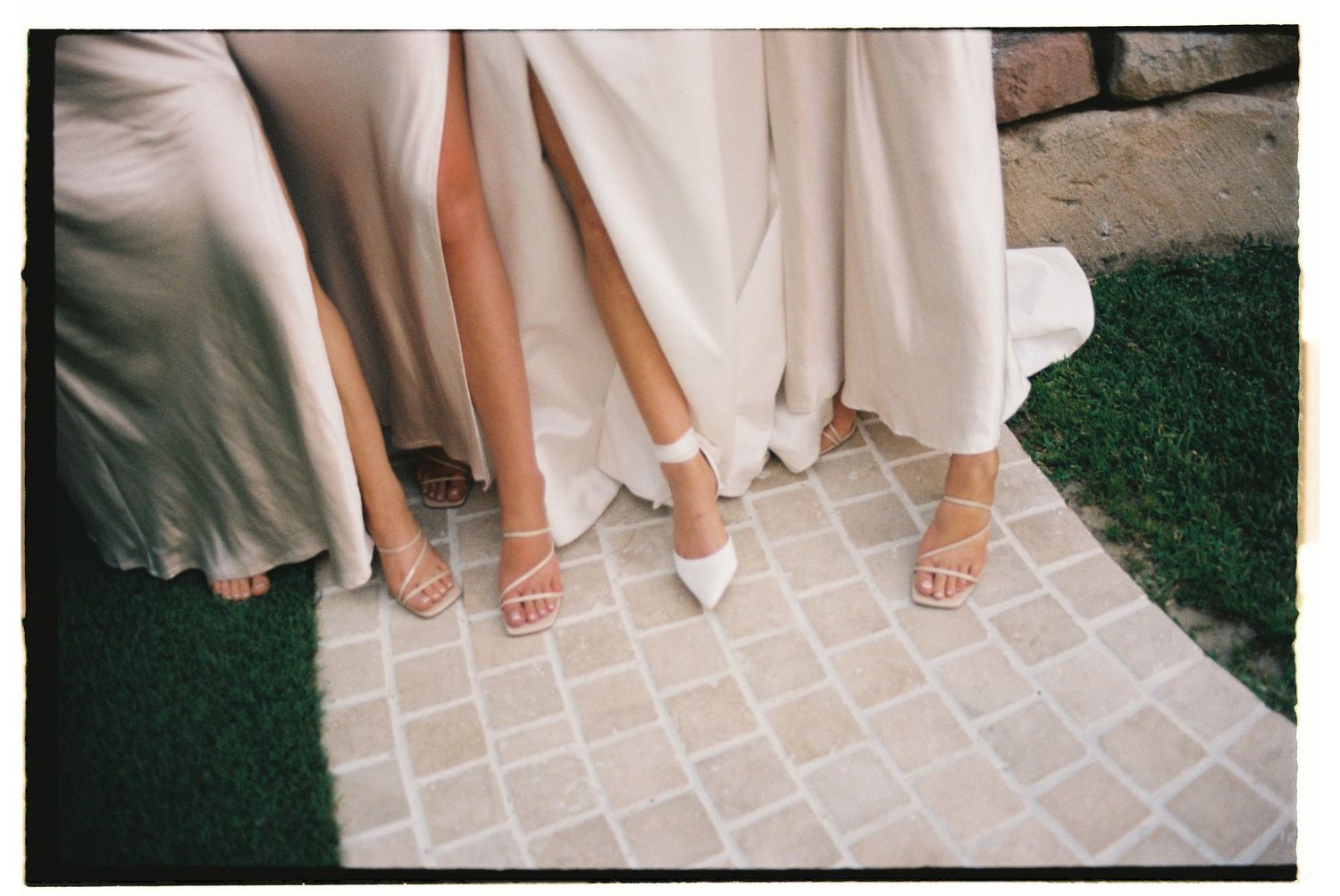 Close-up of bride and bridesmaids showing their heels and dress hems on tiled wedding venue pathway.