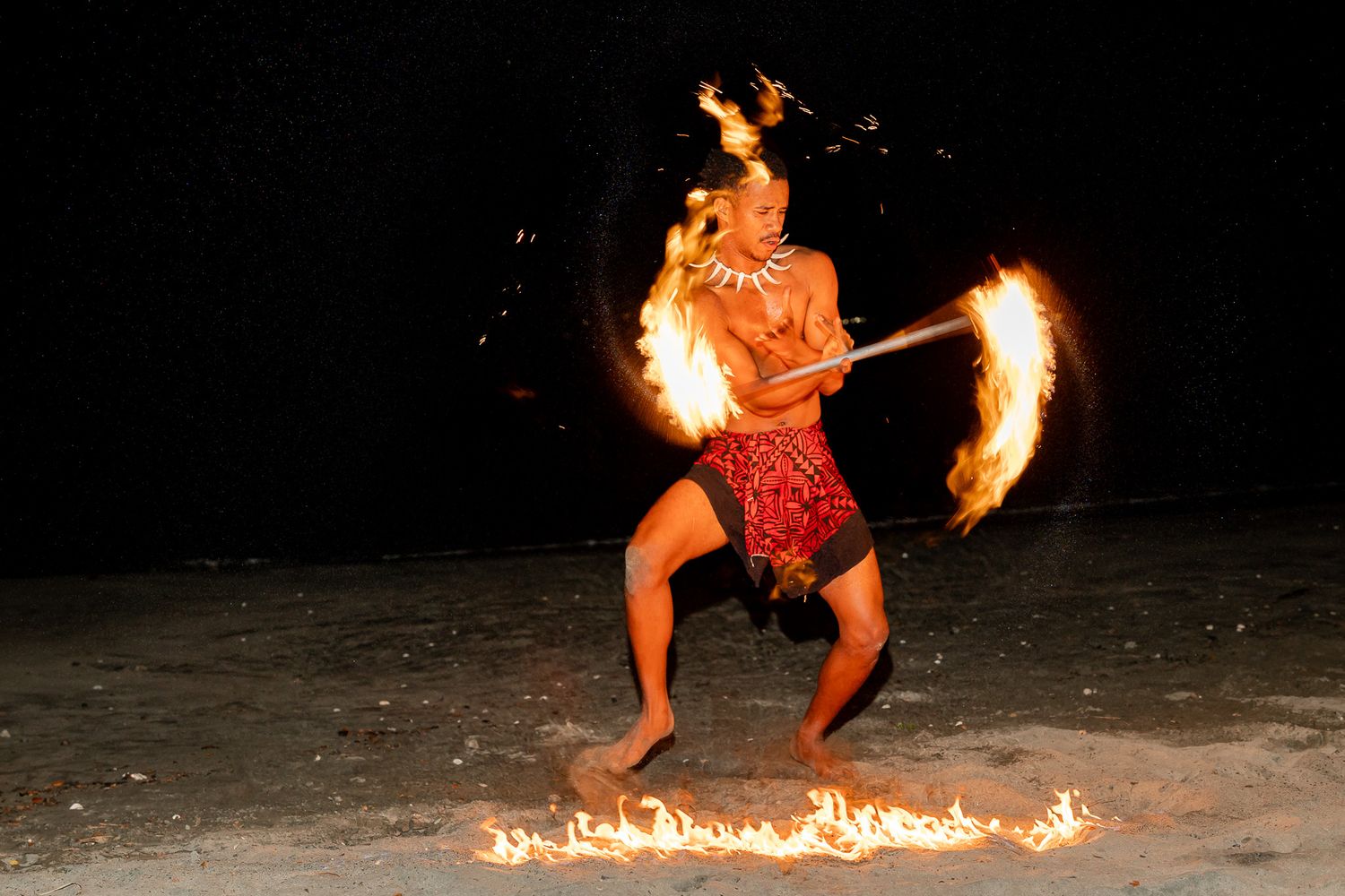 Fire dancer performs dramatic fire spinning show on beach at night during wedding reception.