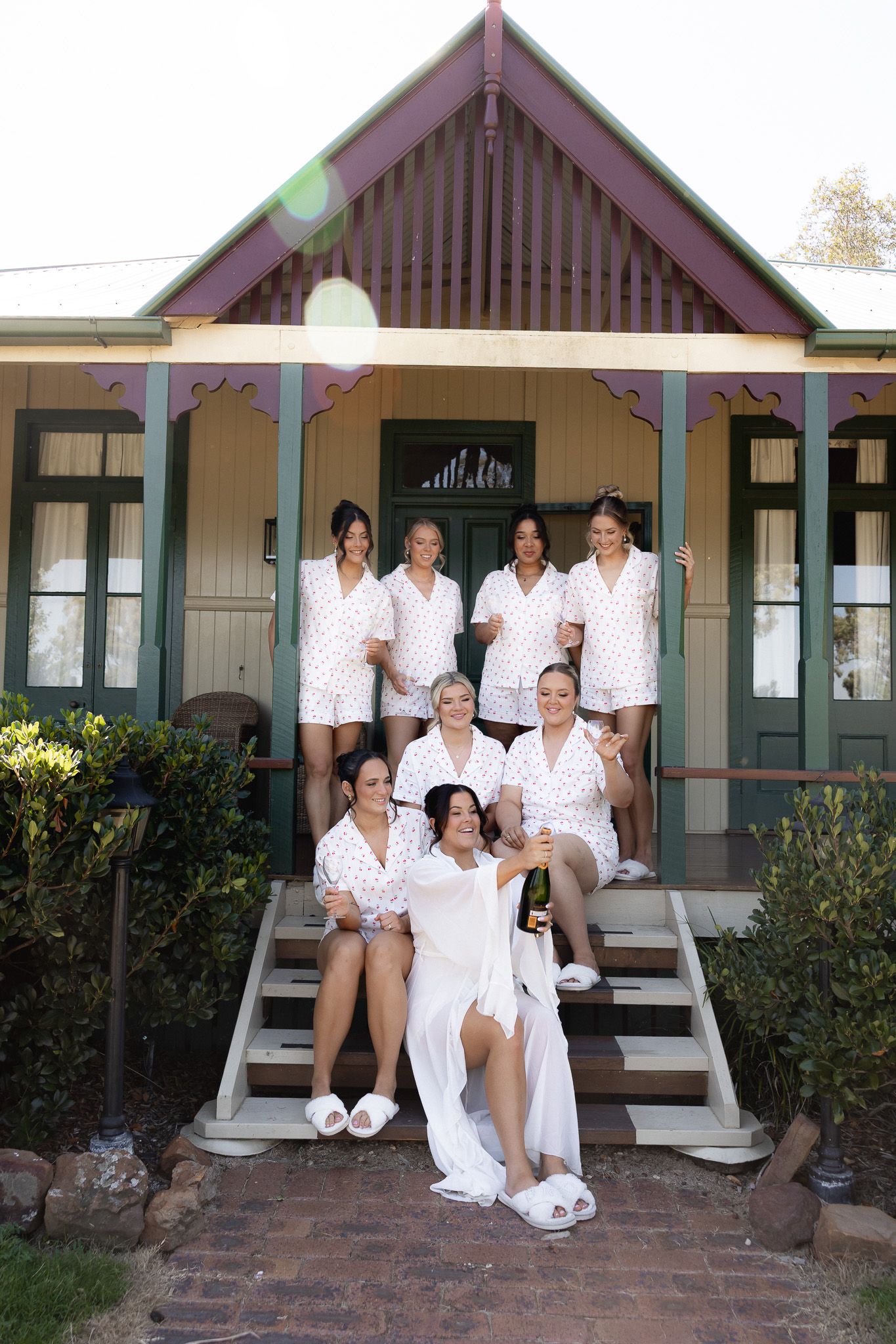 Bride and bridesmaids in matching floral robes celebrating with champagne on cottage steps.