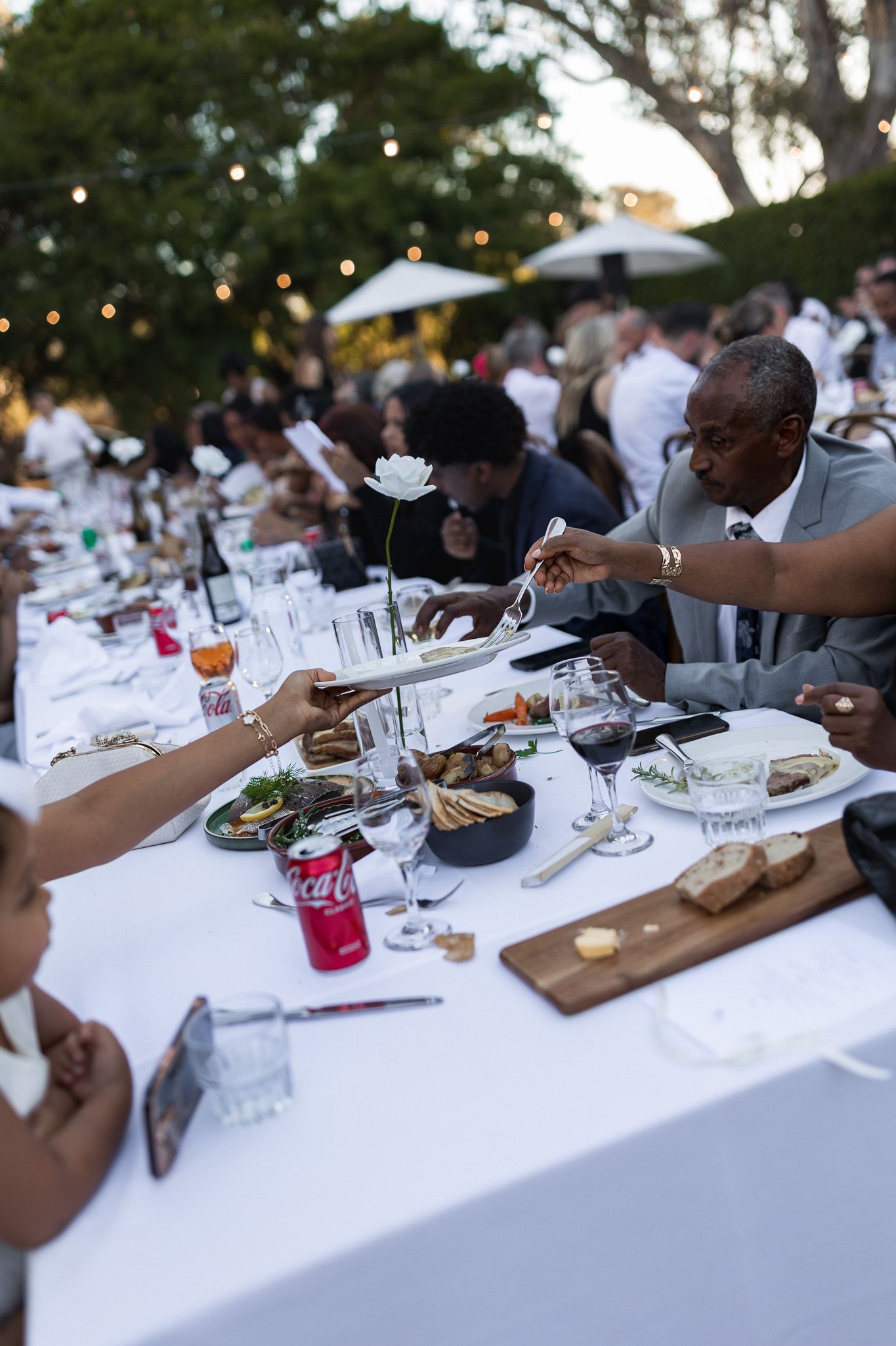 Guests dining at elegant outdoor wedding reception with long white tables and string lights.