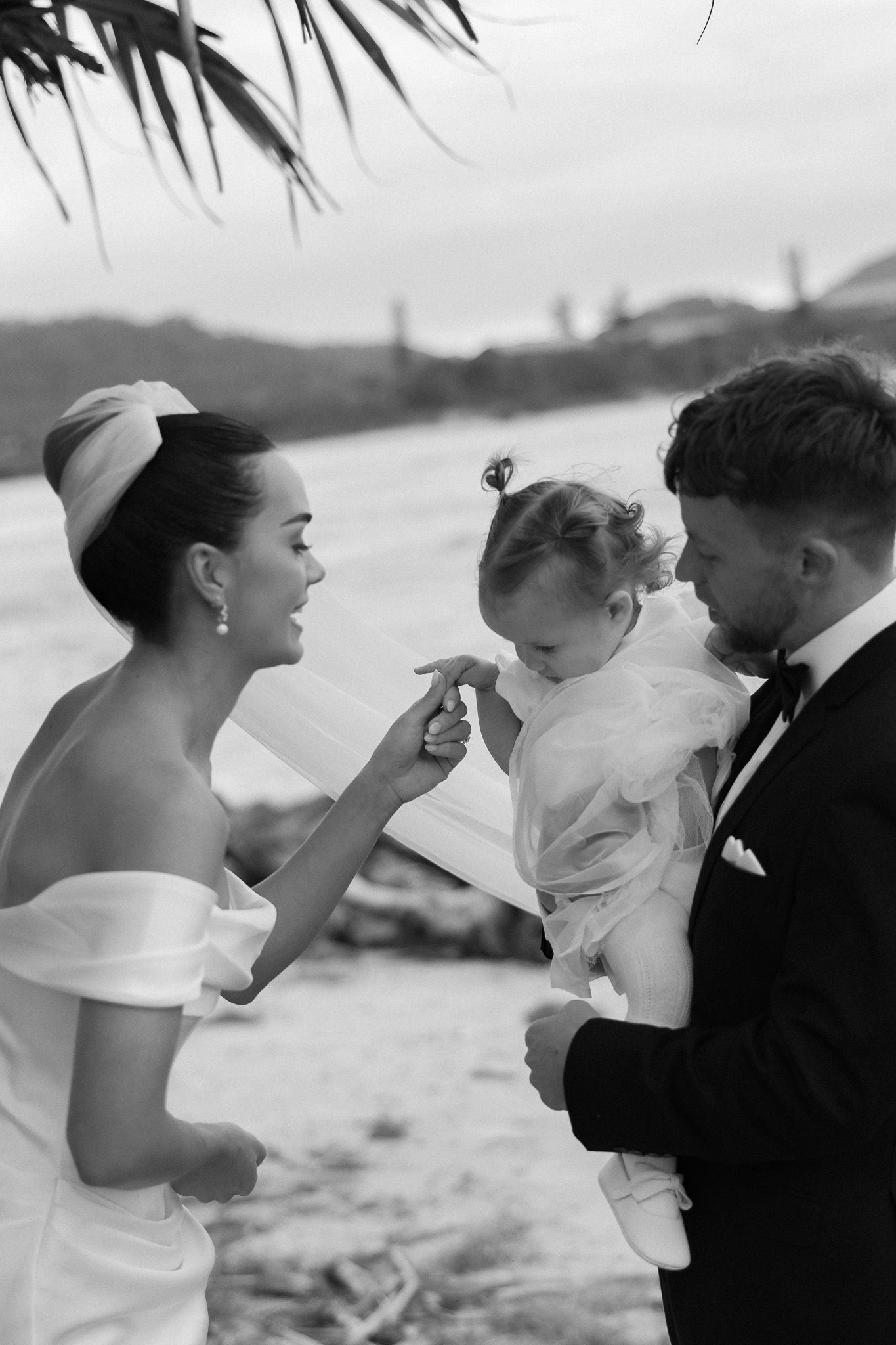 Black and white photo of bride and groom with baby at waterfront wedding.