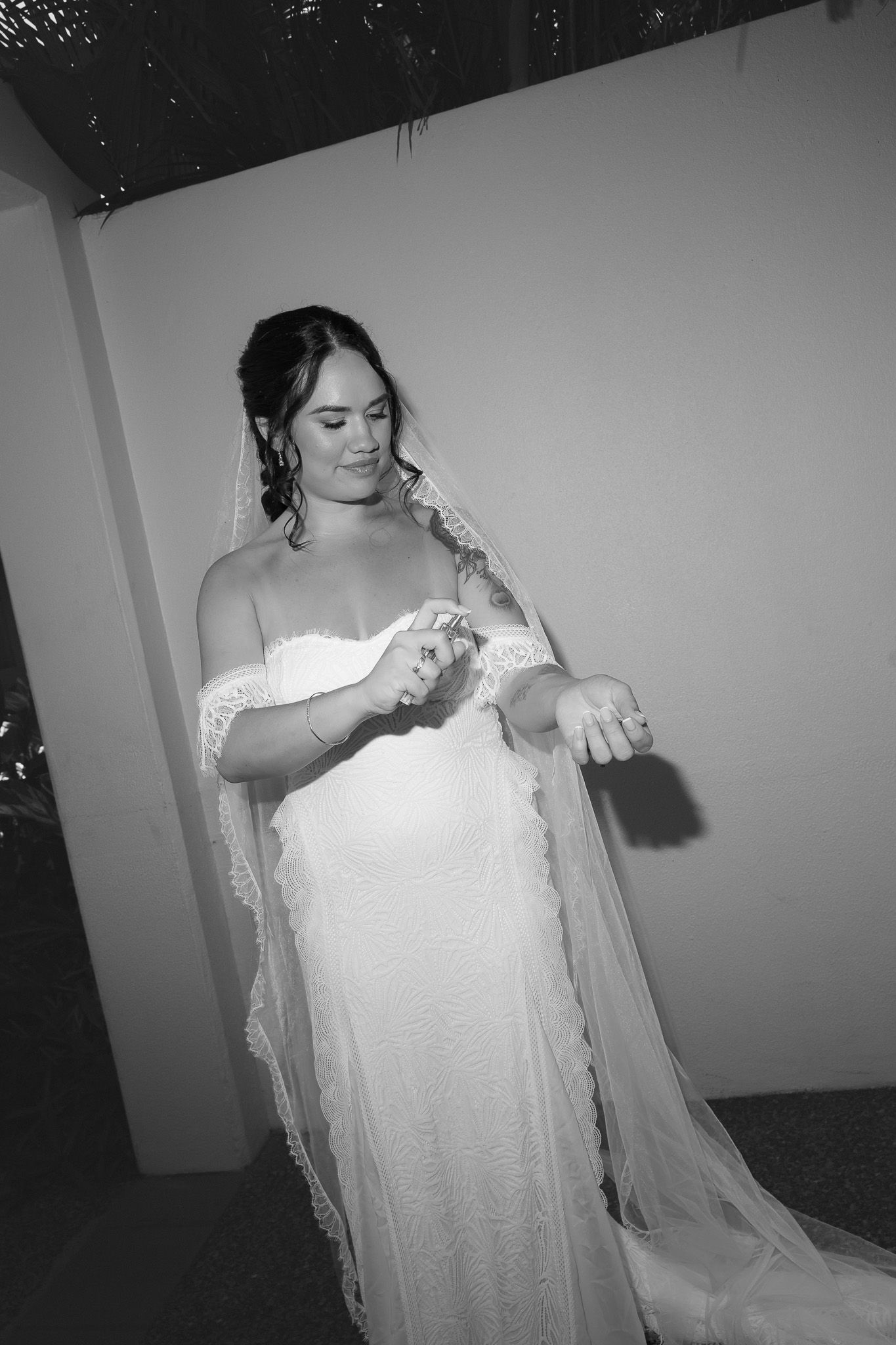 Black and white photo of a bride in a lace wedding dress and veil adjusting her jewelry.